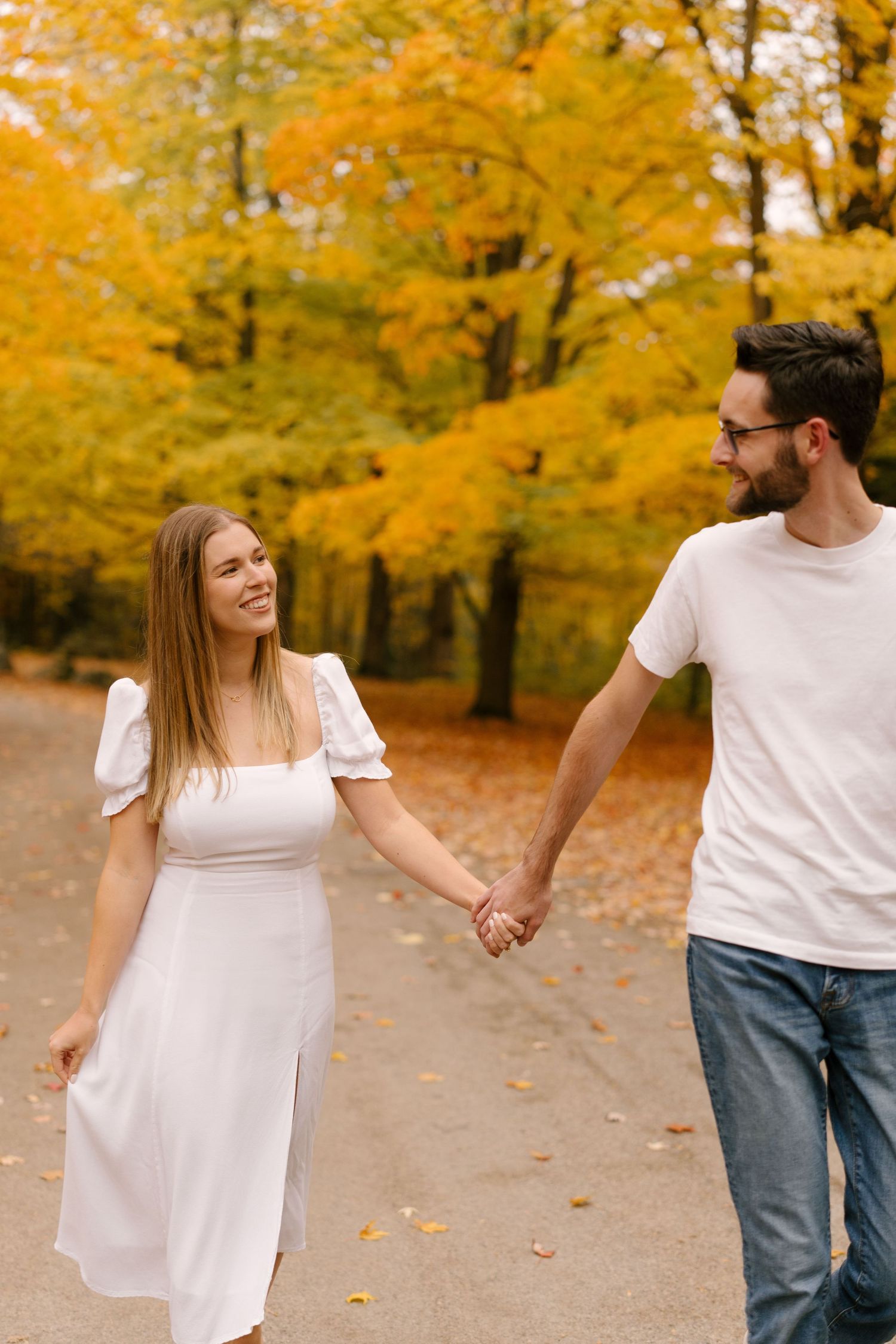 Happy couple holding hands and walking along a path surrounded by vibrant autumn foliage.
