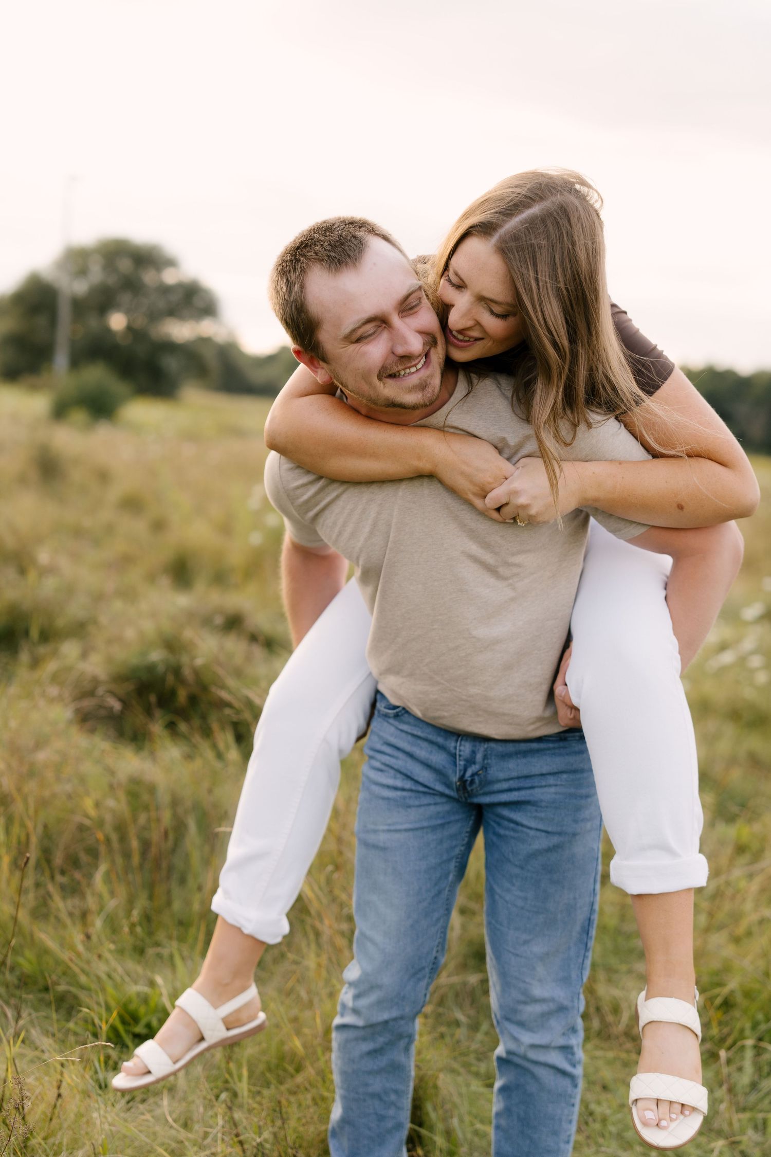 Smiling man giving woman a piggyback ride through a lush green meadow at sunset.