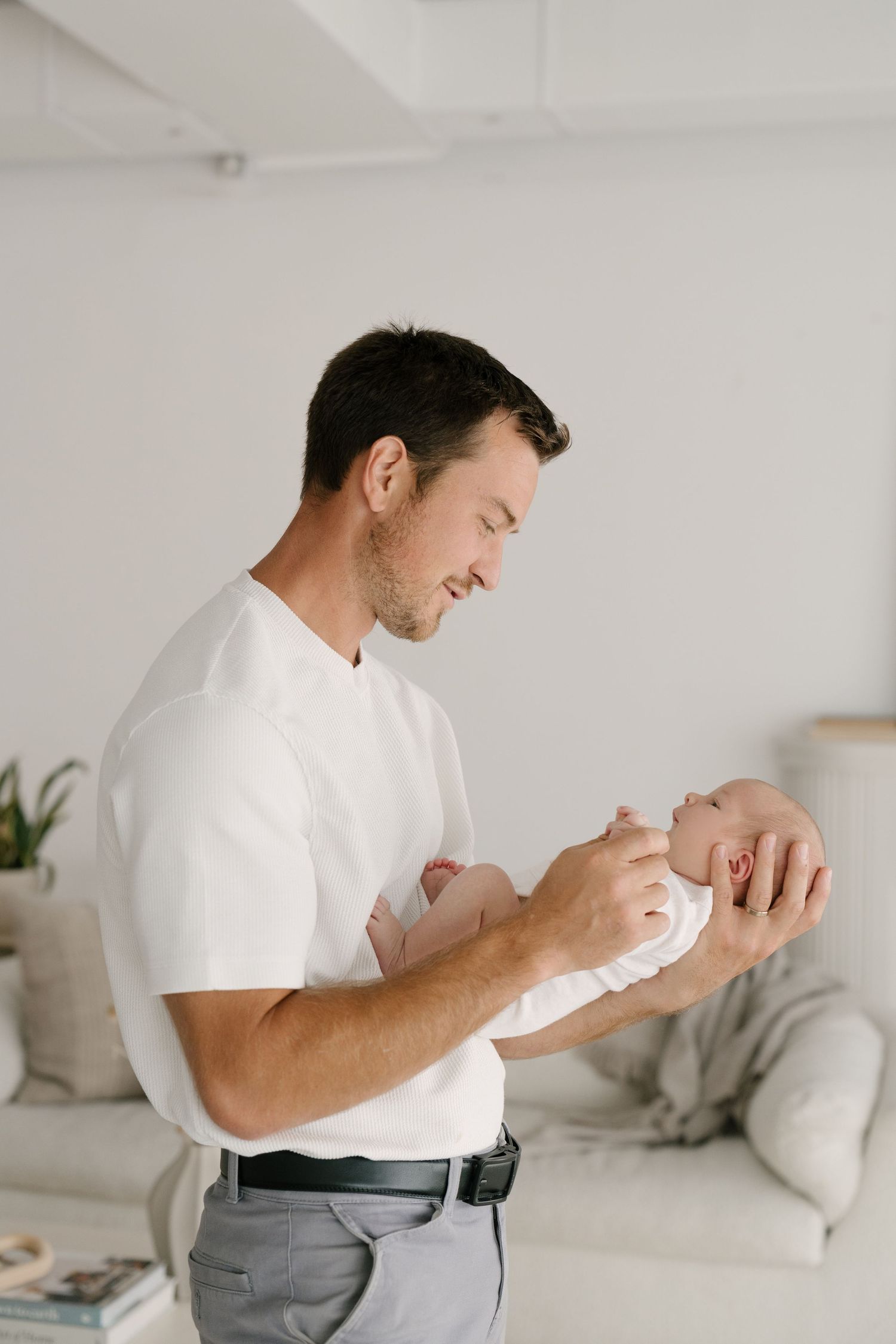 Smiling father in white t-shirt holding newborn baby in bright modern living room.