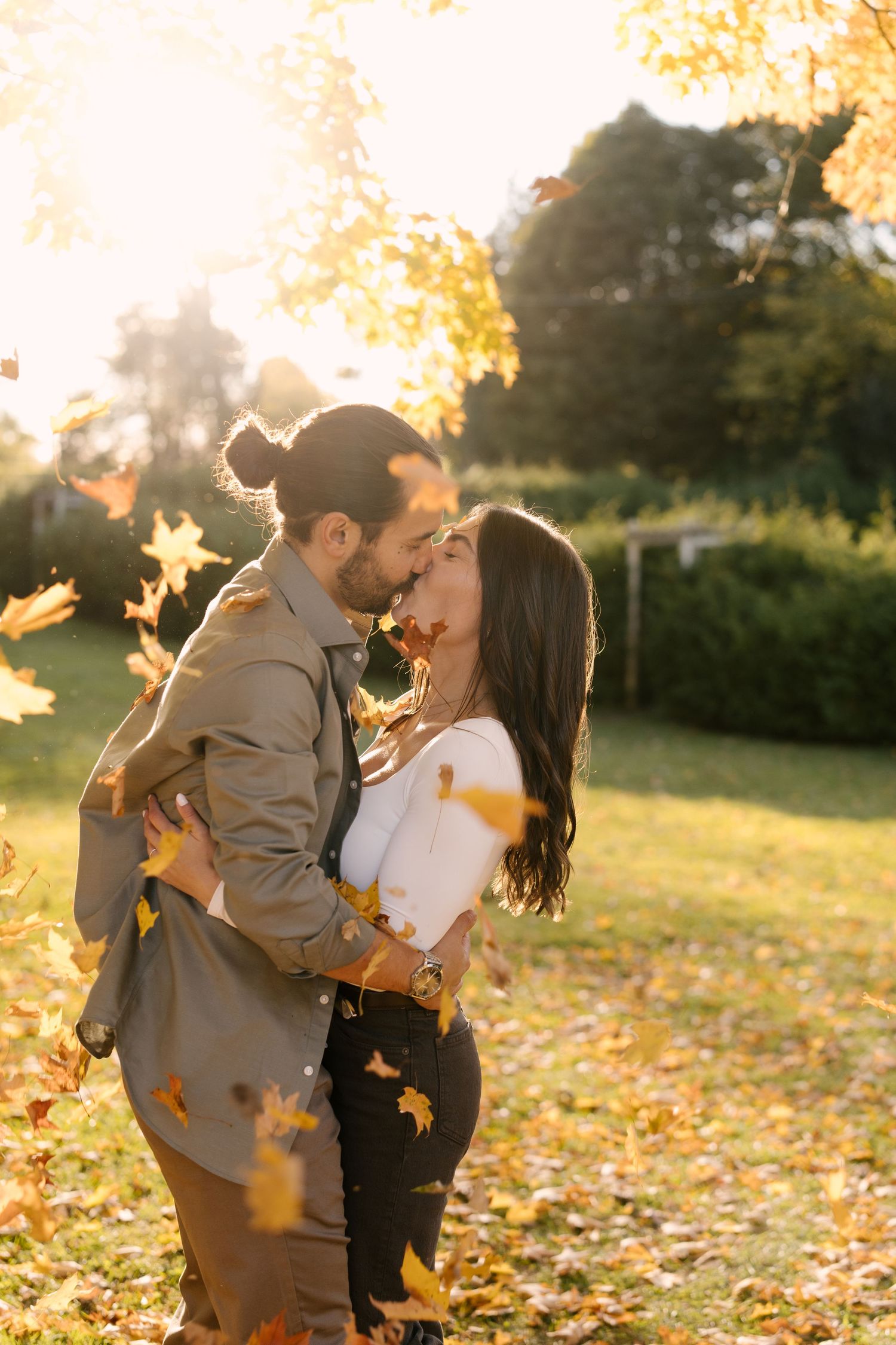 Couple kissing surrounded by falling golden autumn leaves in a sunny park.