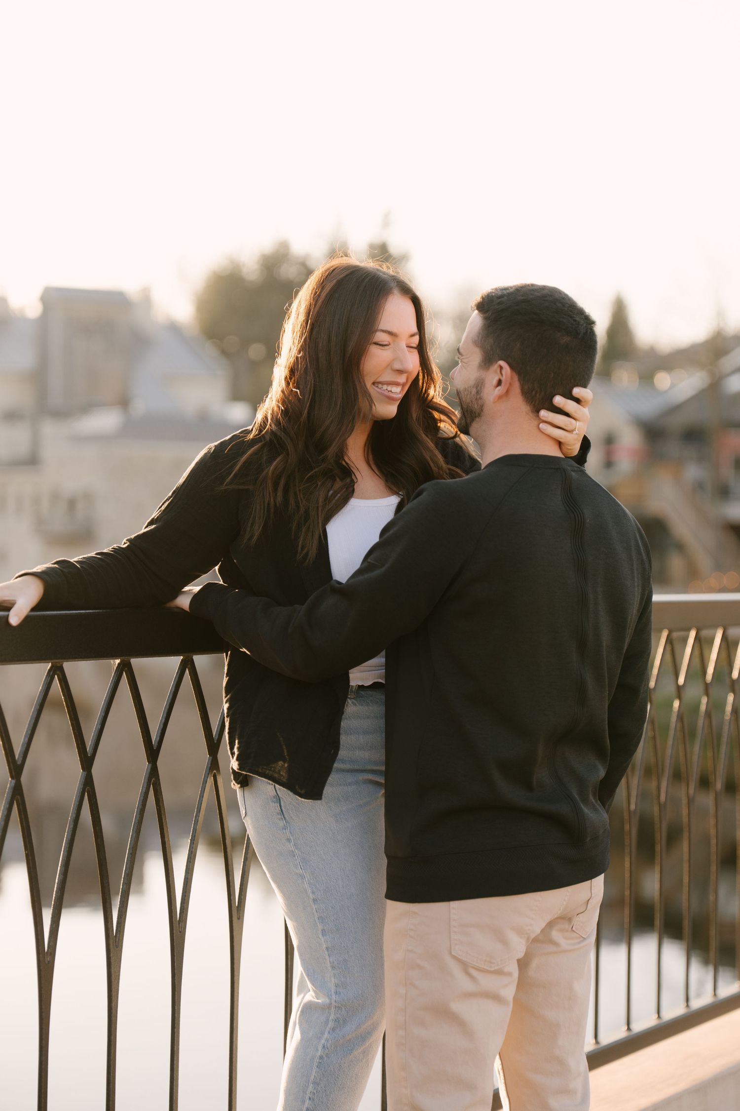Romantic couple sharing a tender moment leaning against a railing at golden sunset.