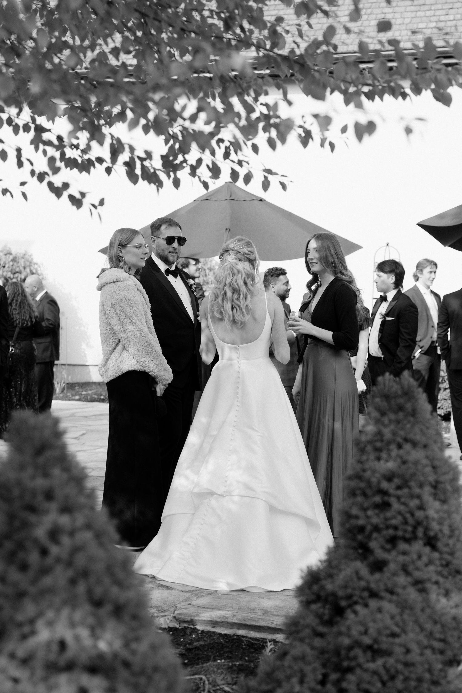 Black and white photo of bride and groom with wedding guests gathered outdoors during cocktail hour.