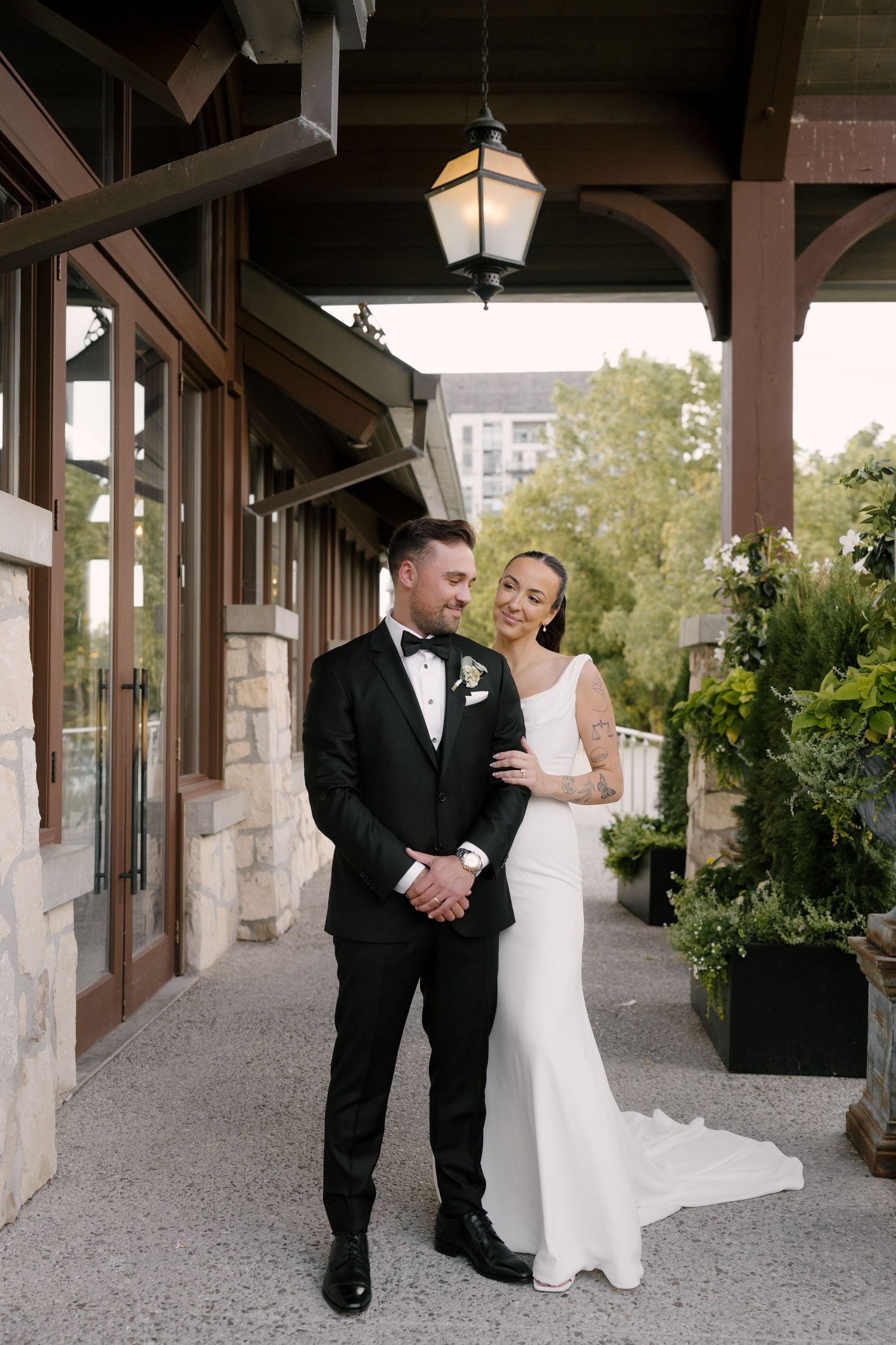 Bride and groom pose elegantly under a wooden pergola with lanterns at an upscale Cambridge Mill venue.