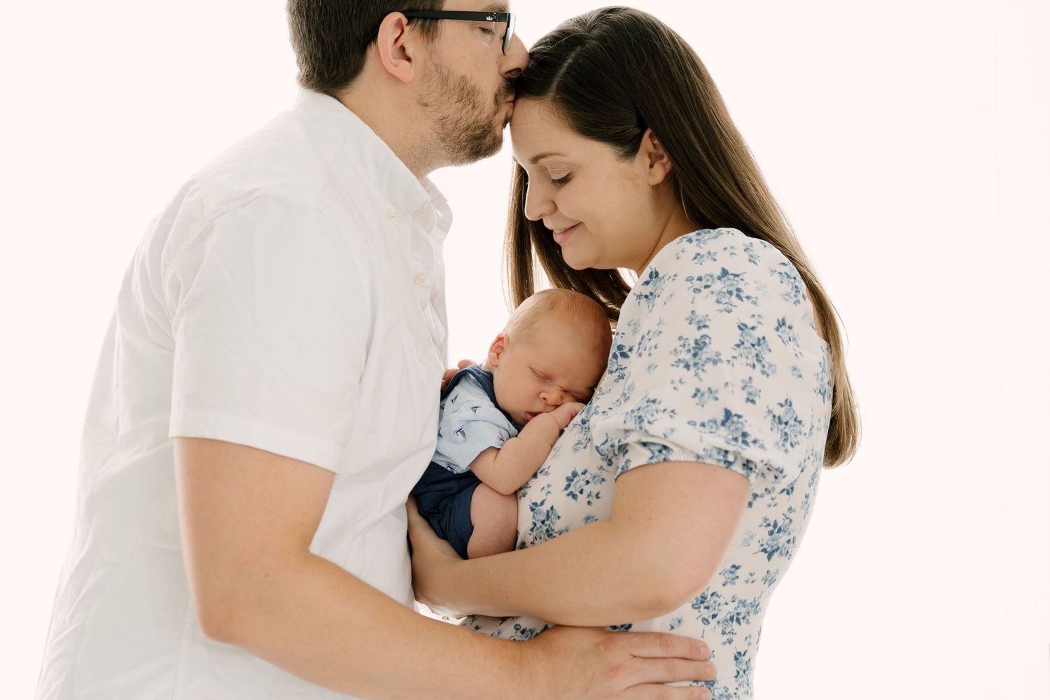 New parents kissing and cuddling while holding their newborn baby close.
