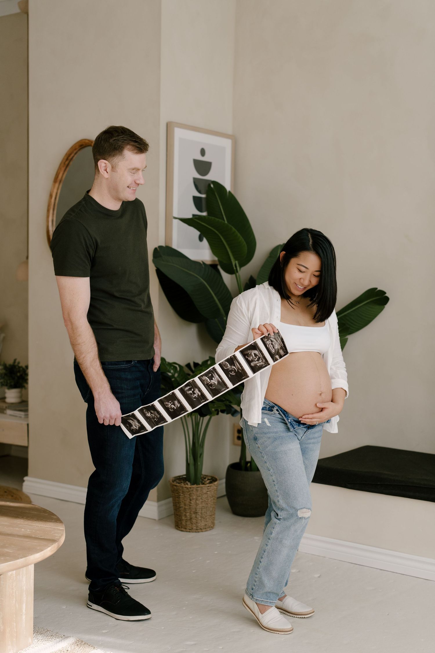 Couple smiling and looking at ultrasound images together in a stylish home with green plants.