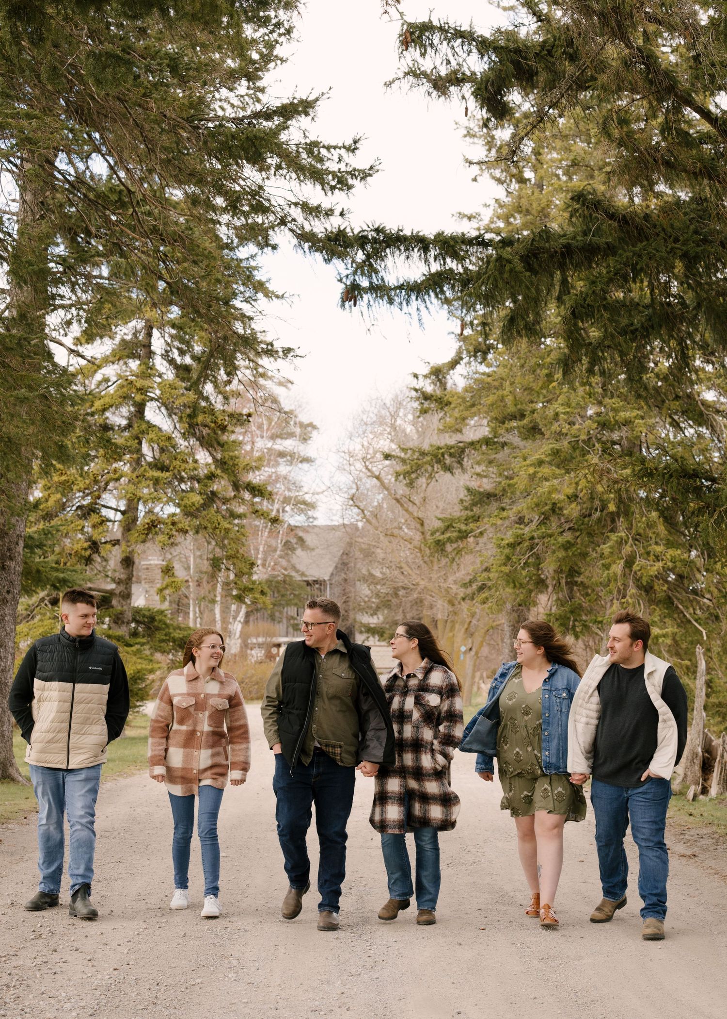 Group of six adults walks along a tree-lined gravel path during an outdoor family photo session.