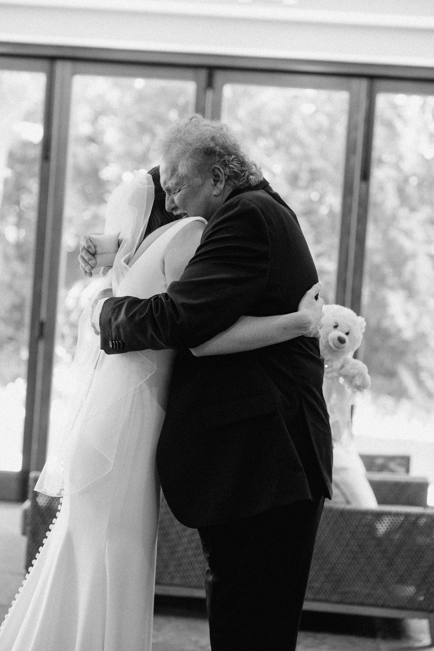 Emotional black and white photo of a bride in a veil sharing a heartfelt hug with an older man at Cambridge Mill.