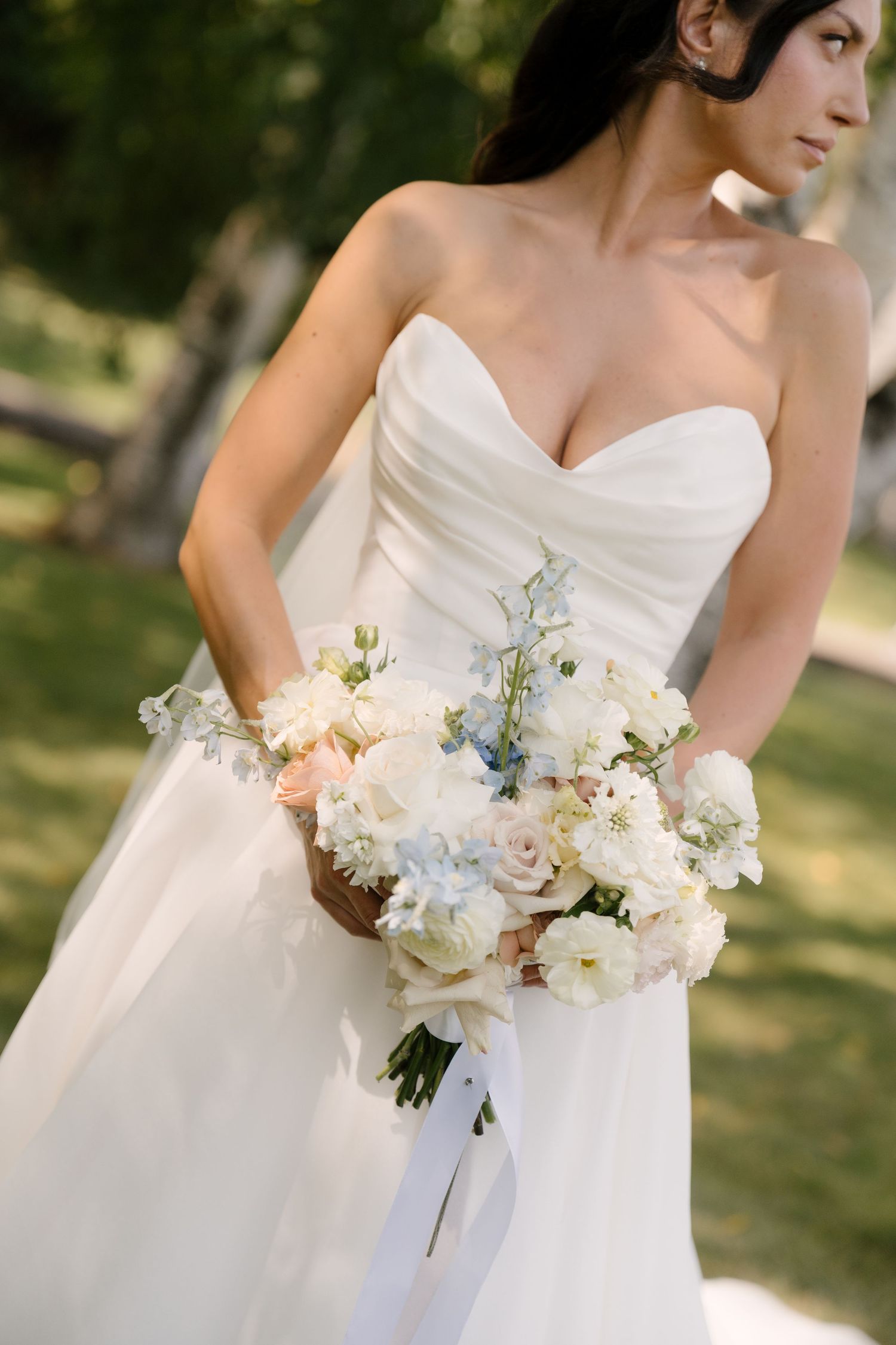 Close-up of bride holding white and blush wedding bouquet in strapless gown.