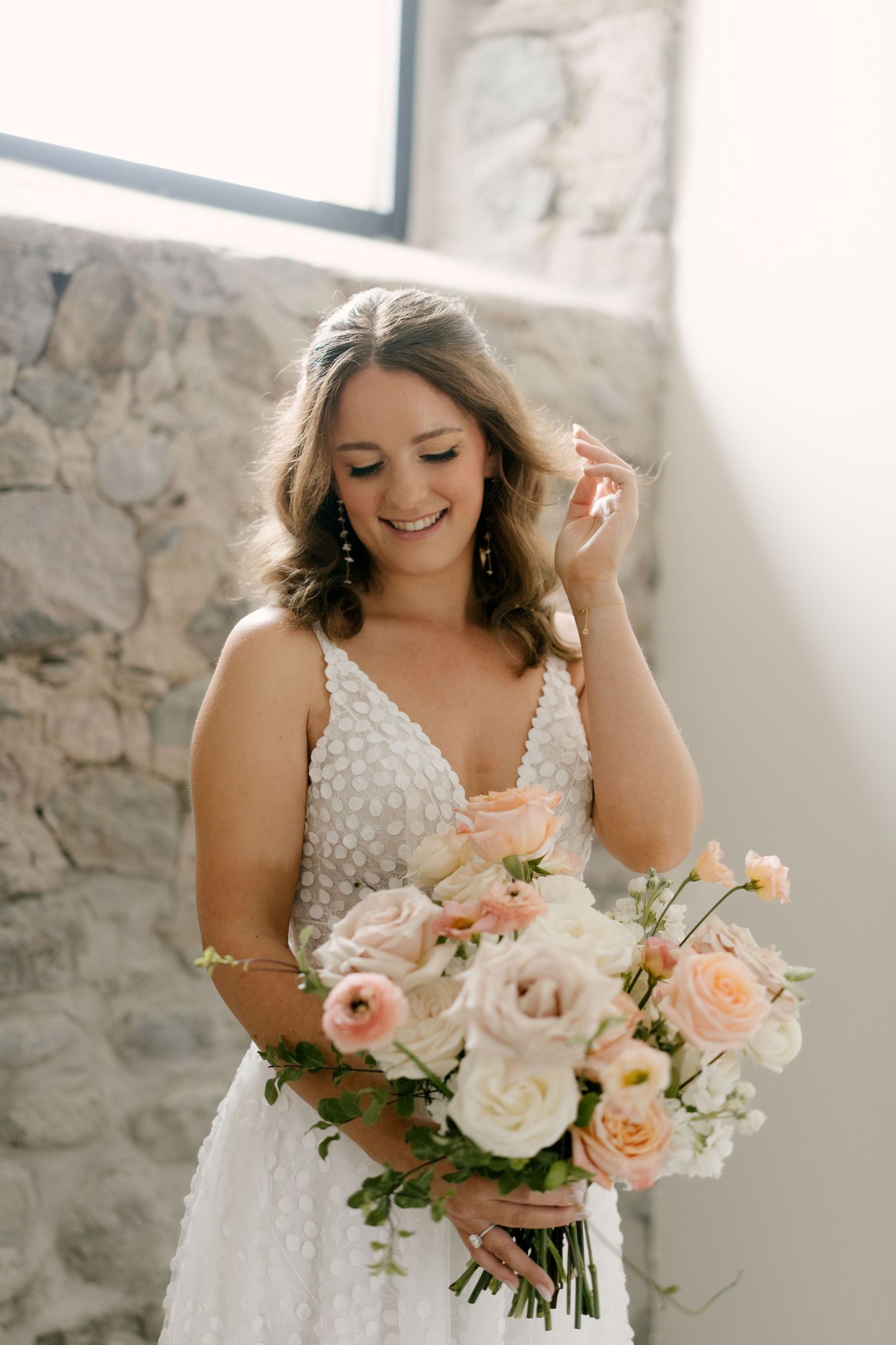 Radiant bride in beaded gown holding blush and white rose bouquet near stone wall window in Wakefield Estates.