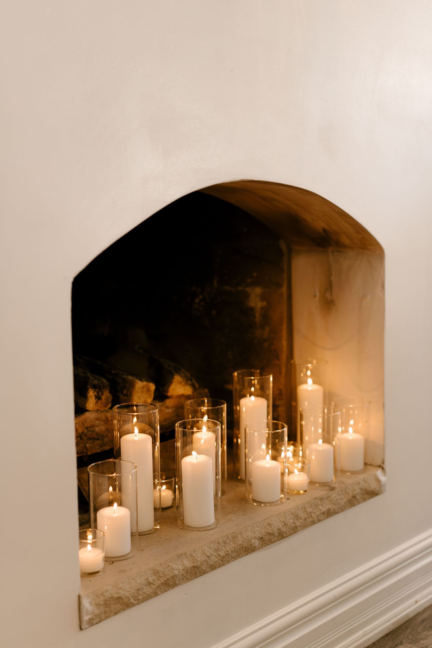 A cozy fireplace filled with glowing white pillar candles in glass holders creates warm wedding ambiance.