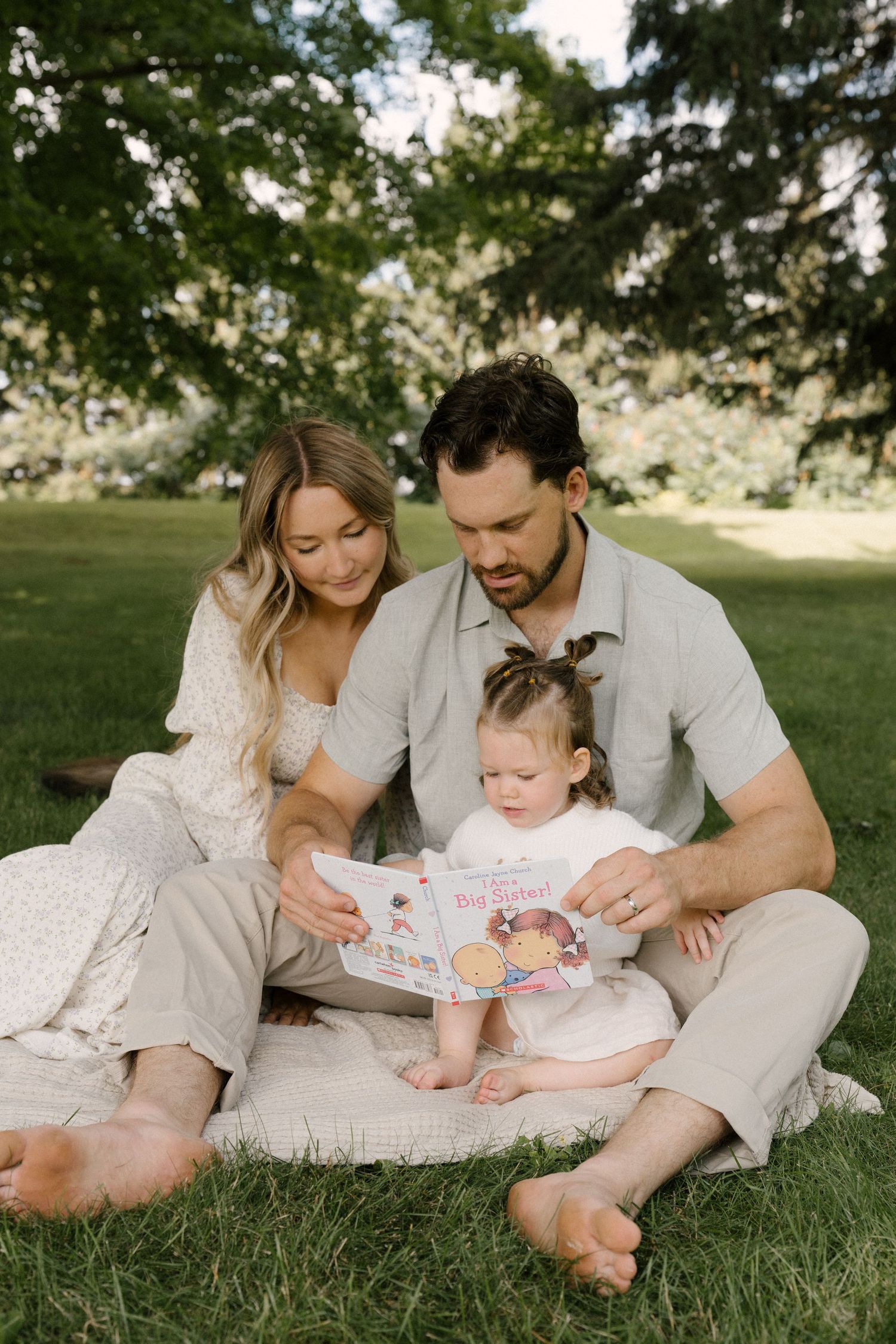 Family sitting on grass reading a children's book together outdoors.
