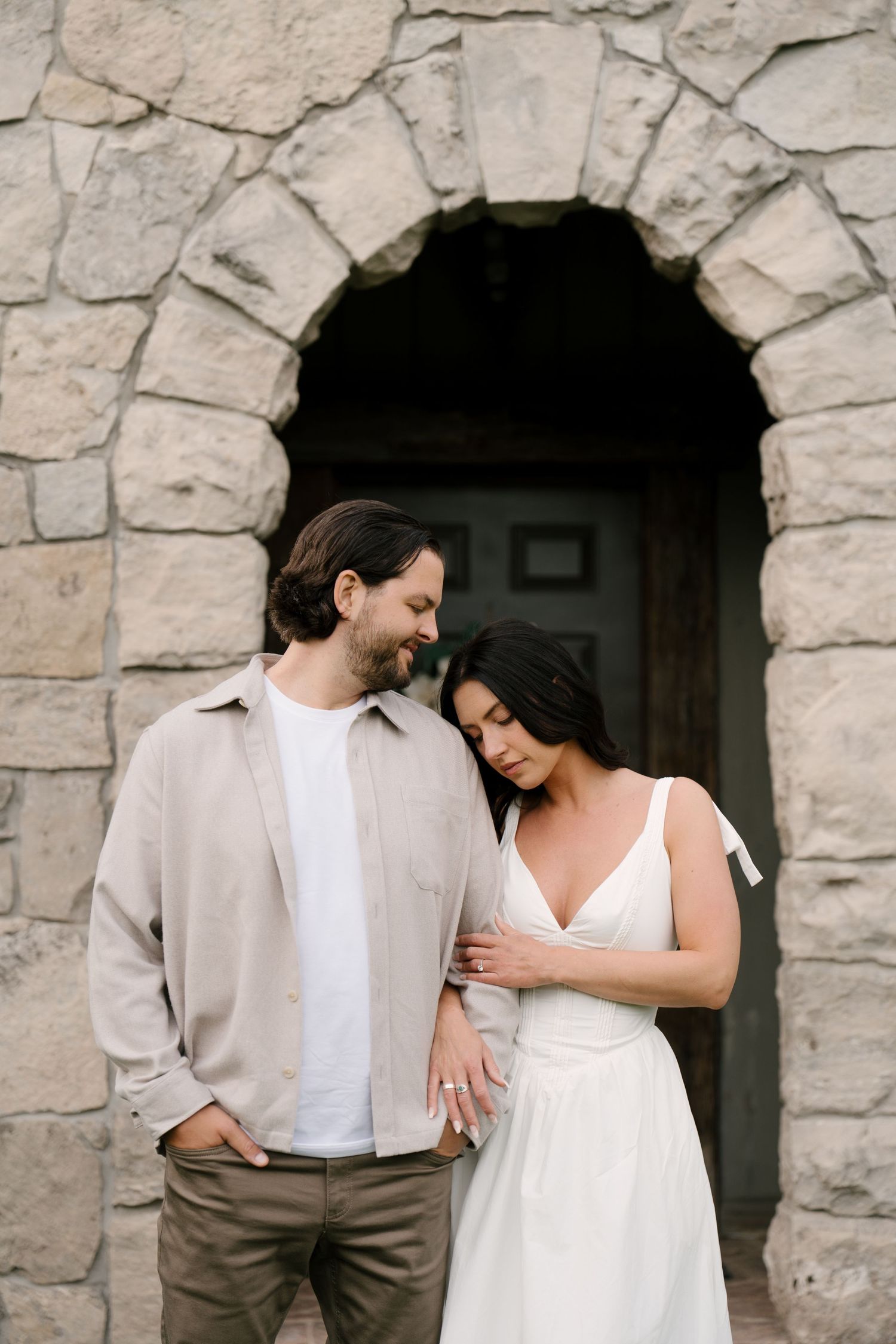 Couple embracing tenderly in front of rustic stone arch doorway on their wedding day.