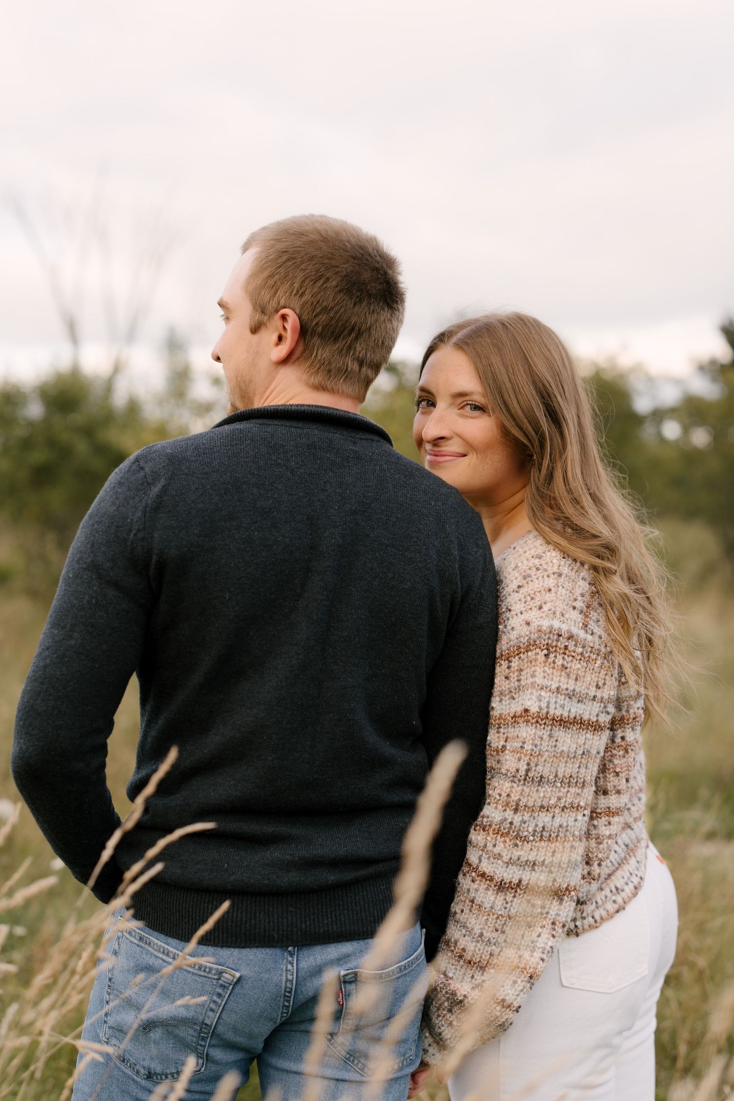 Woman leaning against man's shoulder smiling at camera in a golden autumn field.