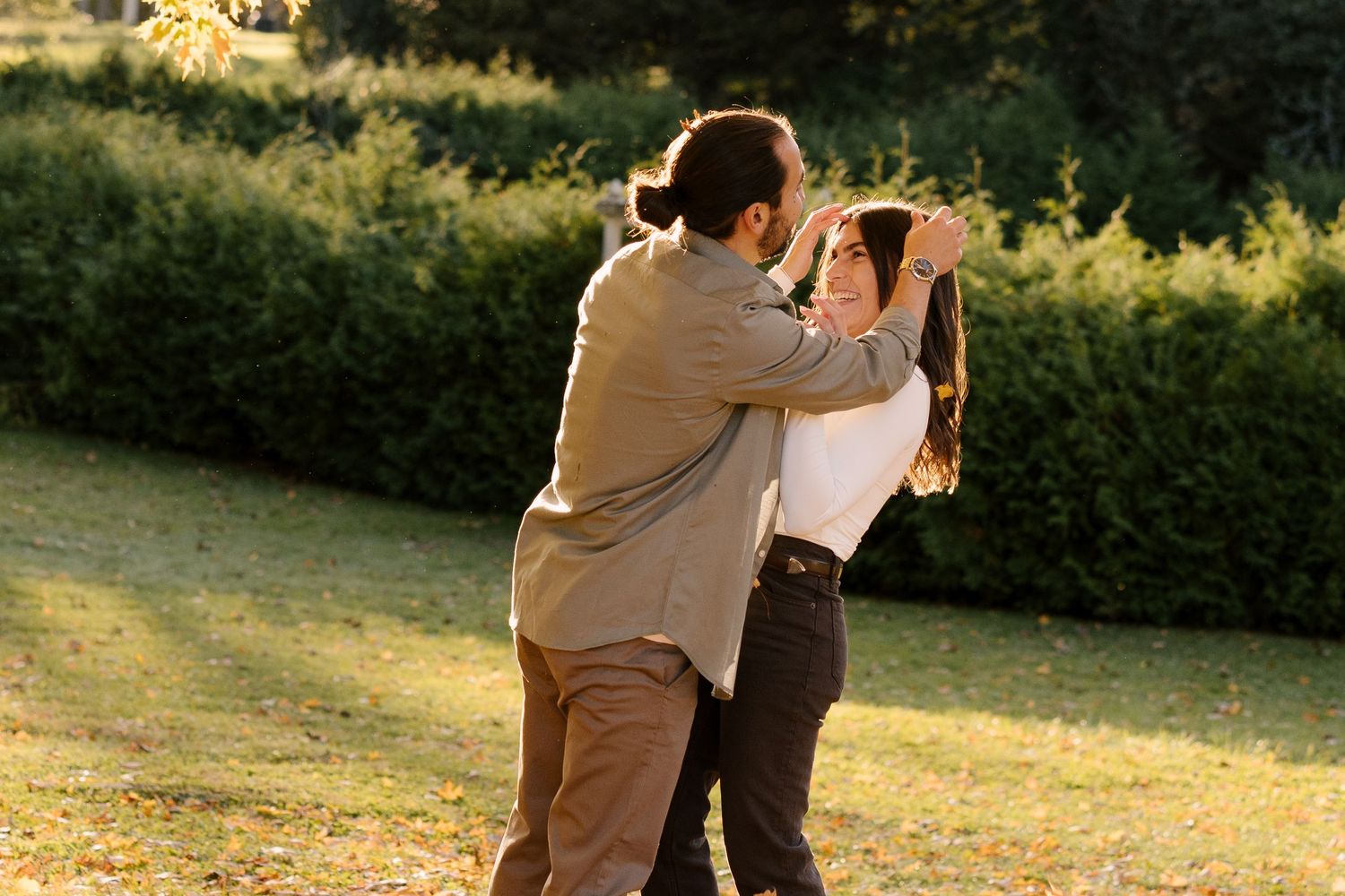 Couple dancing and embracing in a sunlit park with lush green hedges in the background.