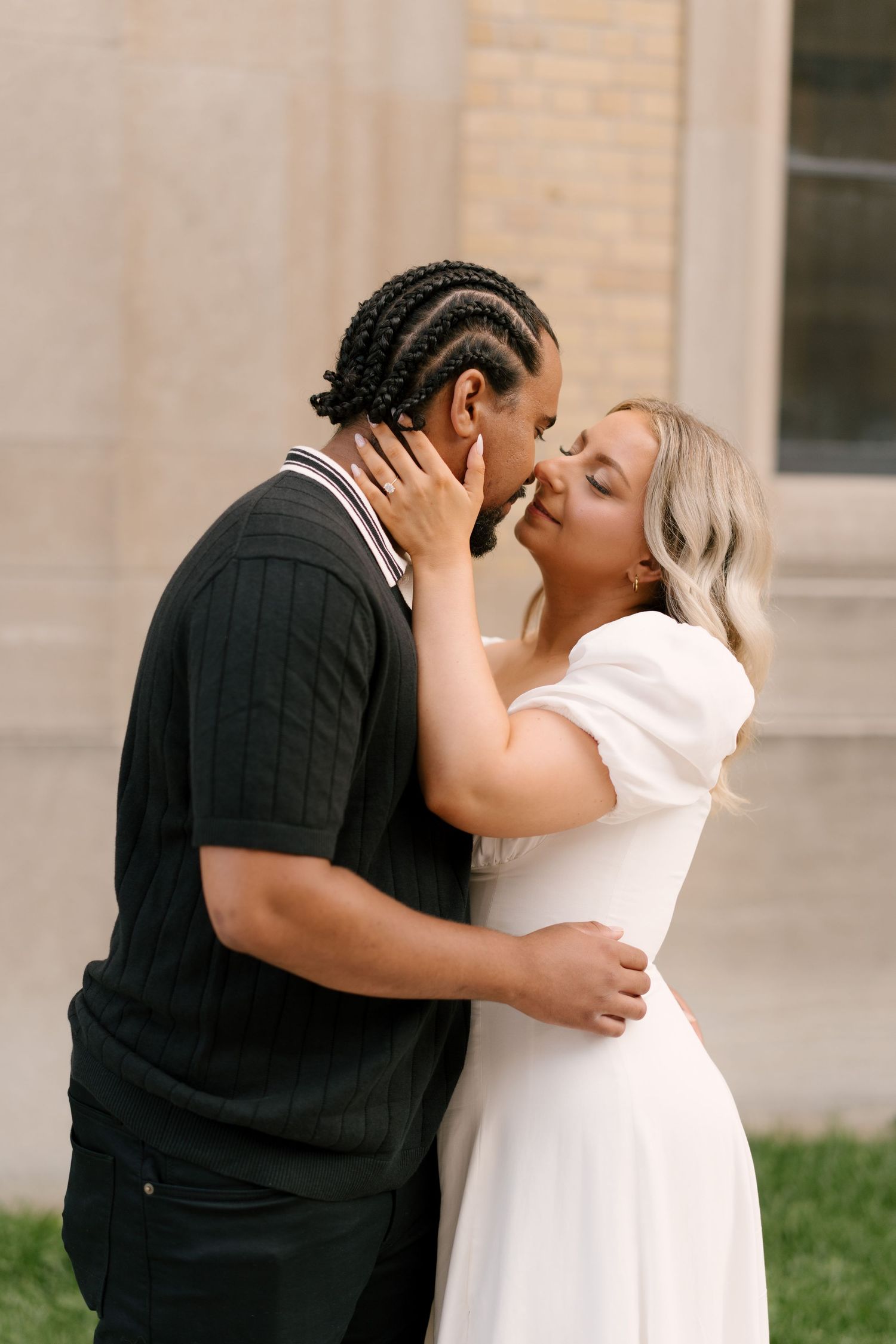 Interracial couple sharing a passionate kiss outdoors near a stone building during engagement session.