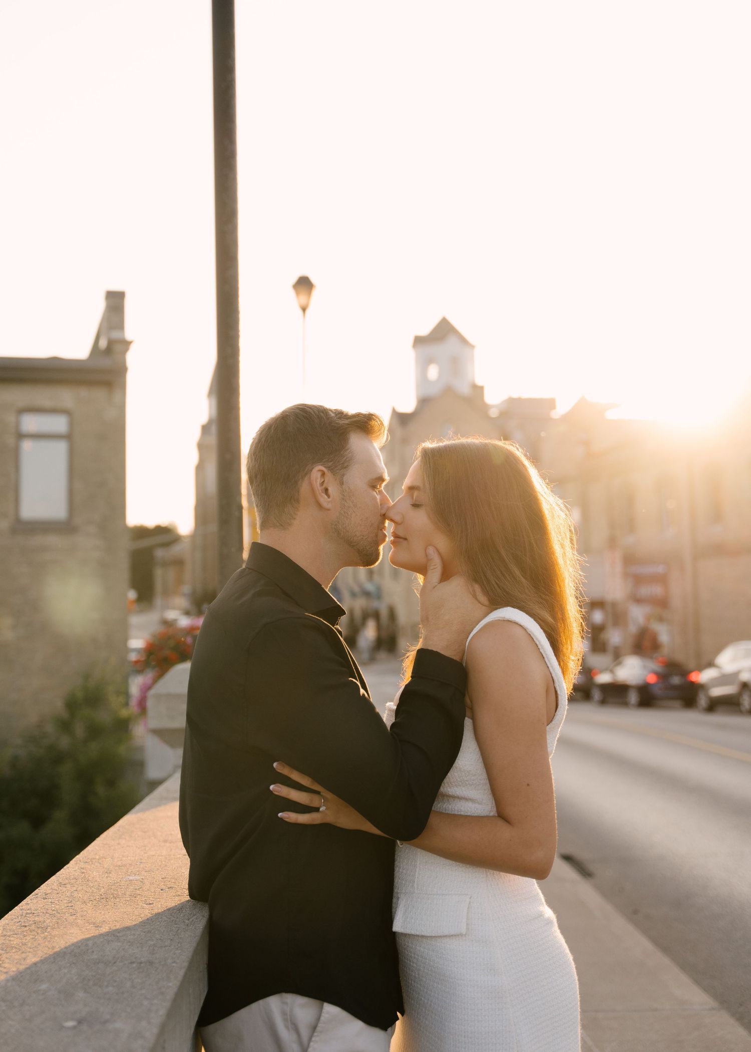 Romantic couple nearly kissing at golden sunset on urban street bridge.