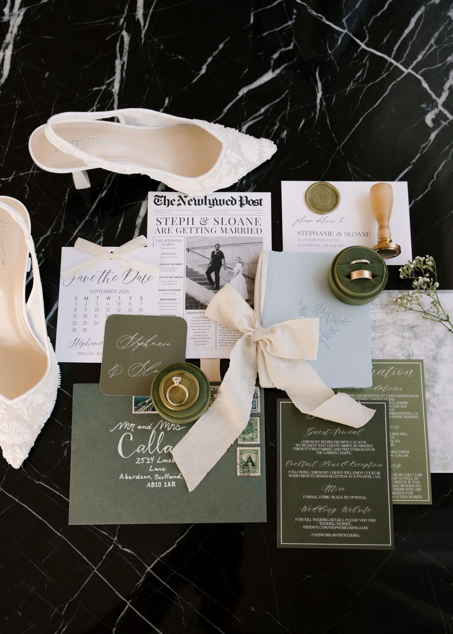 Wedding flat lay featuring invitations, rings, white heels, wax seal, and sage green stationery.