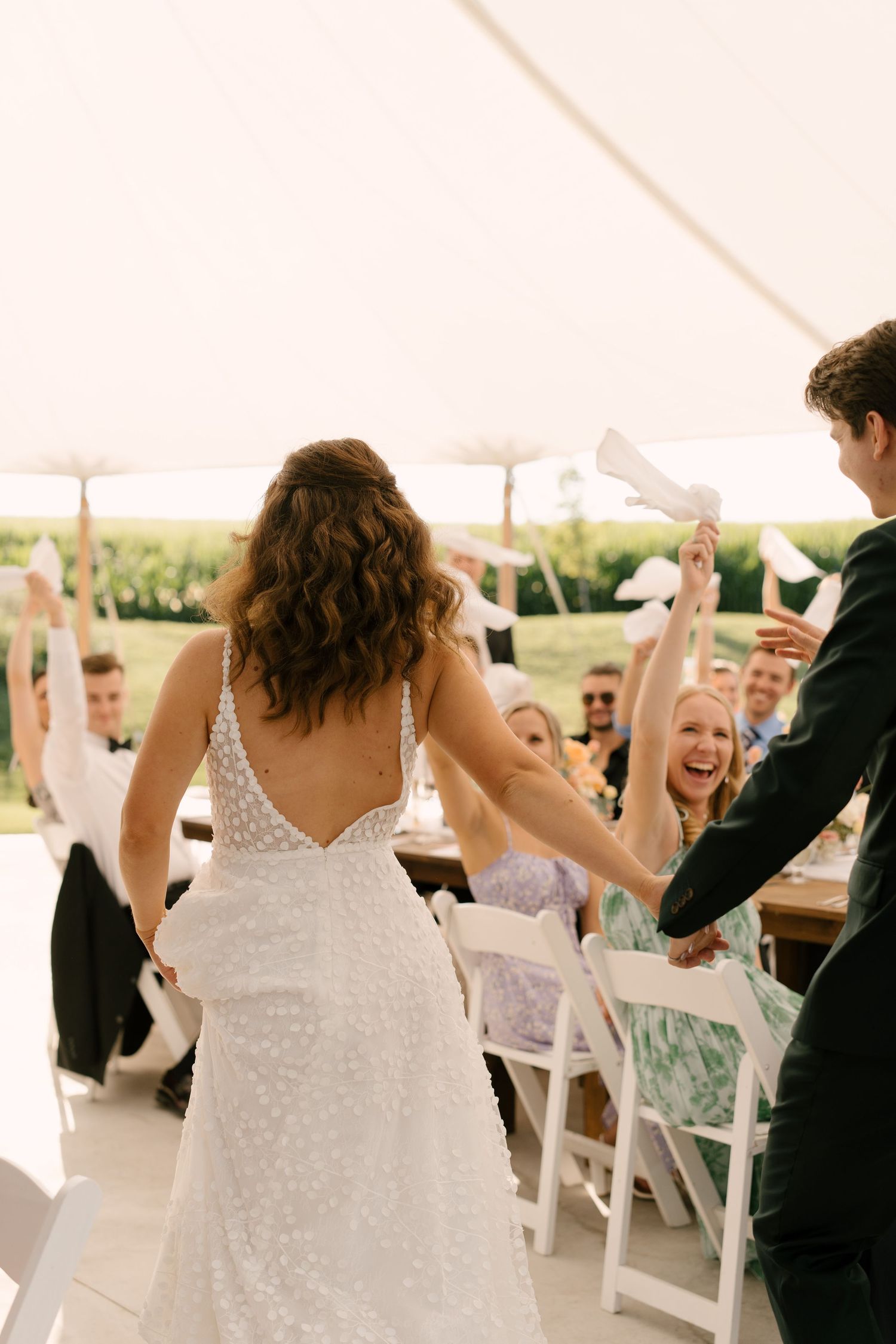 Bride and groom make grand entrance as cheering guests wave napkins at outdoor Wakefield Estates tent reception.