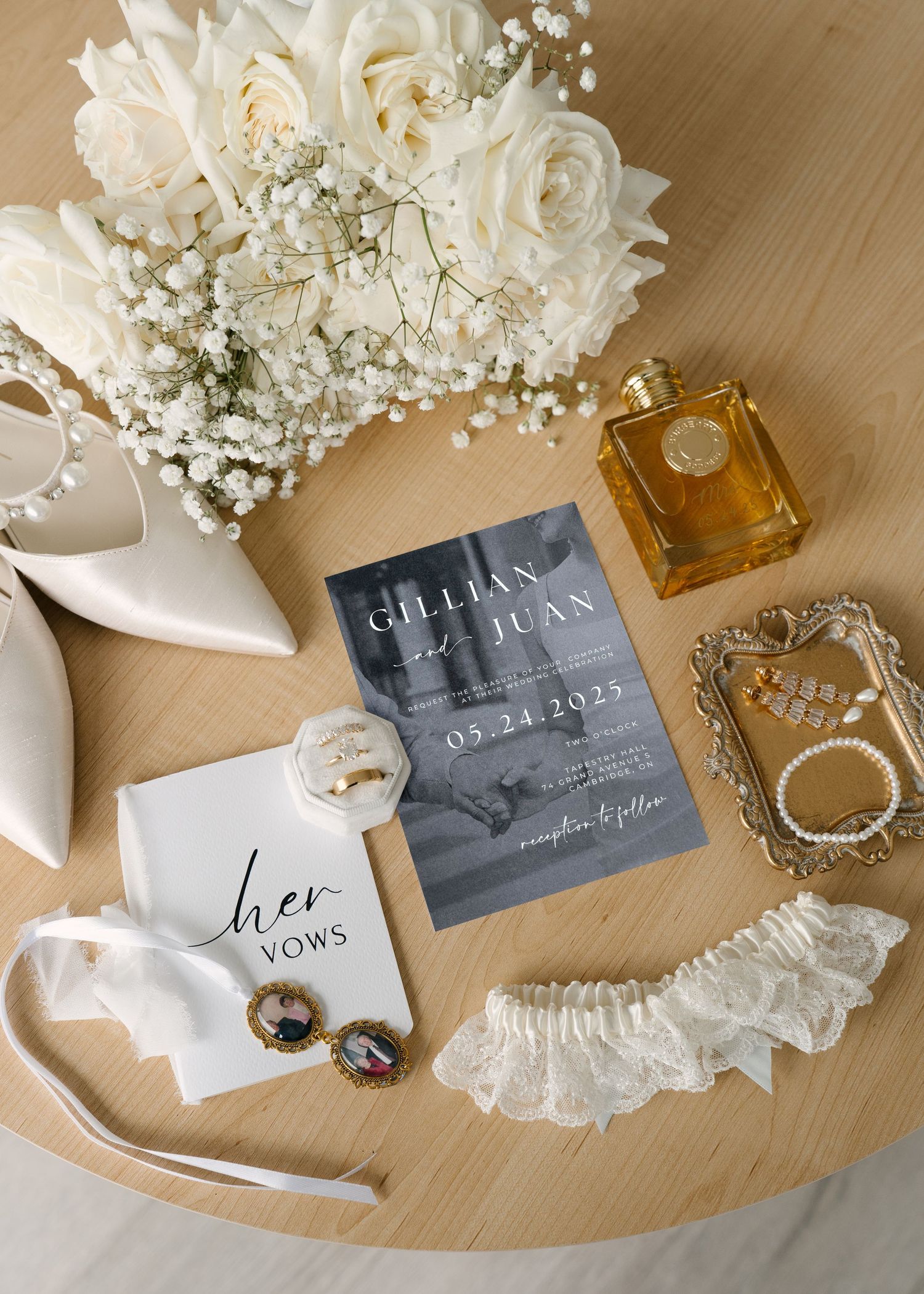 Wedding flat lay featuring invitation for Gillian and Juan, bridal shoes, bouquet, perfume, vow book, and lace garter.