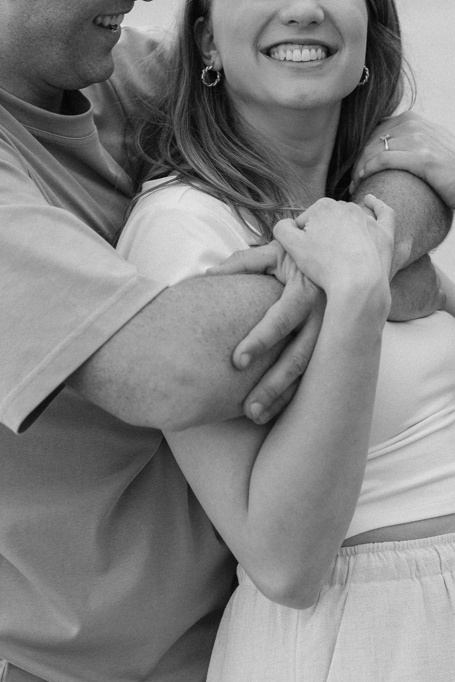 Black and white close-up of smiling woman being embraced from behind by partner.
