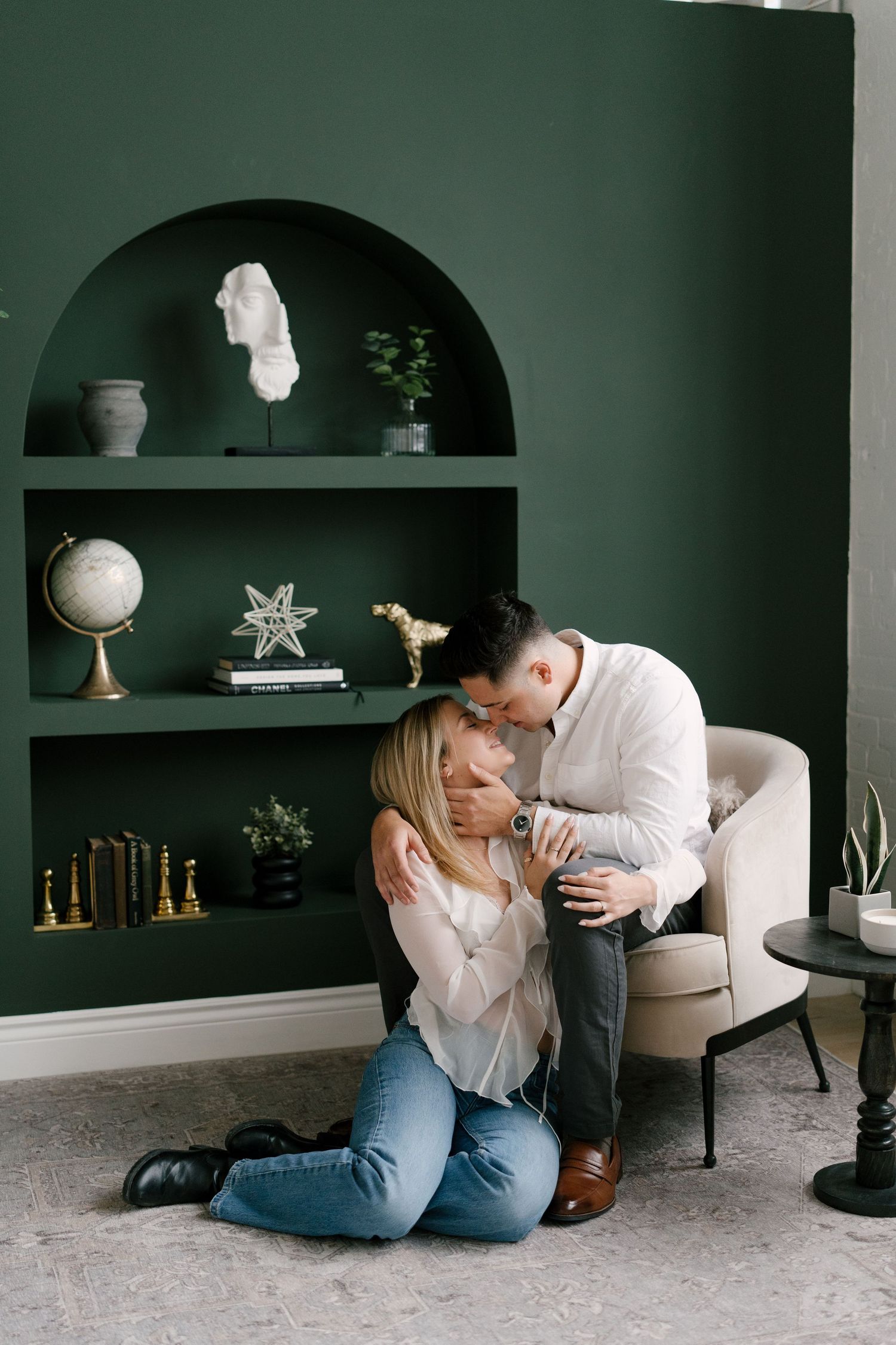 Man in white shirt embracing woman kneeling on floor in a stylish green-walled living room.