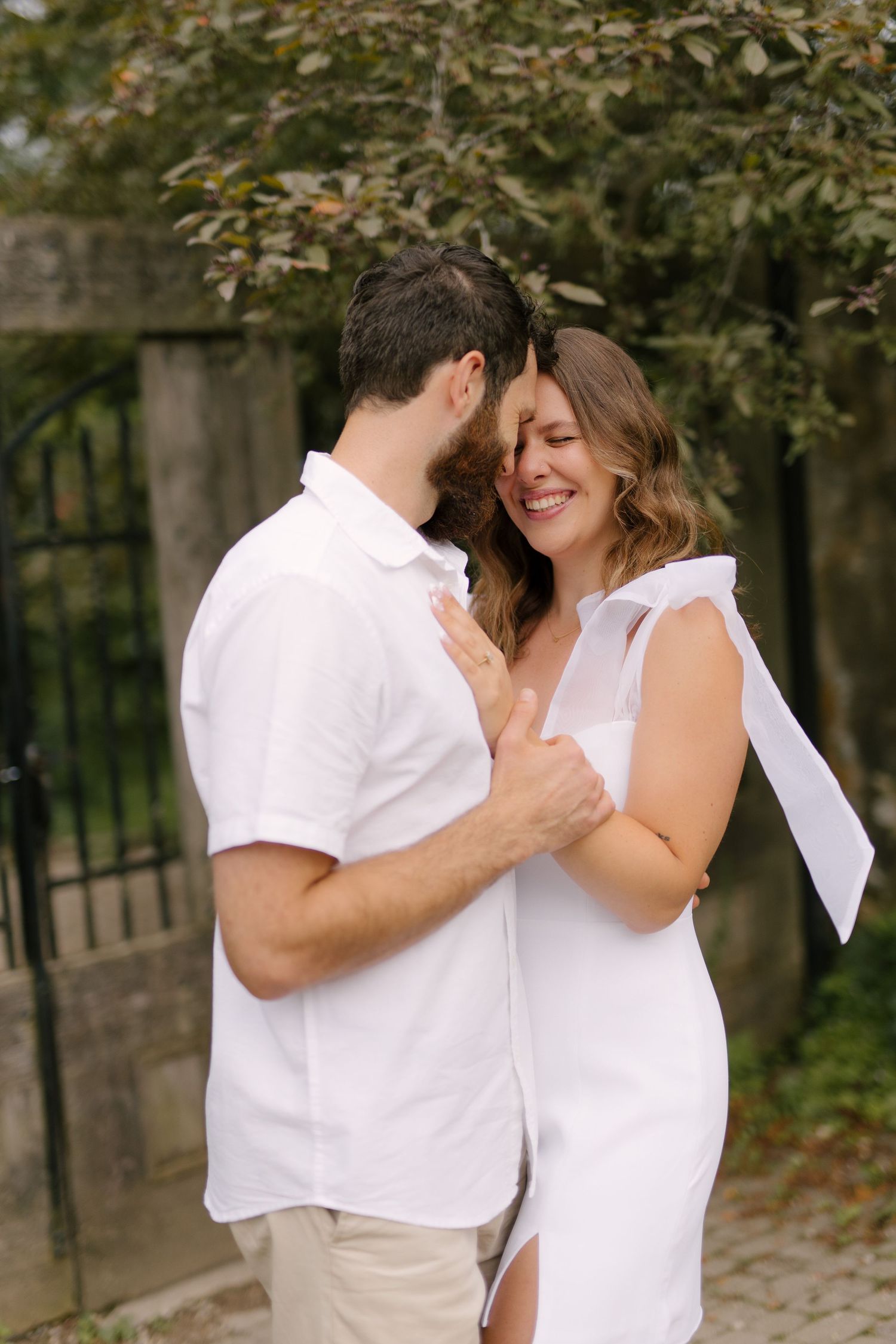 Couple in matching white outfits sharing a tender moment while embracing near a garden gate.