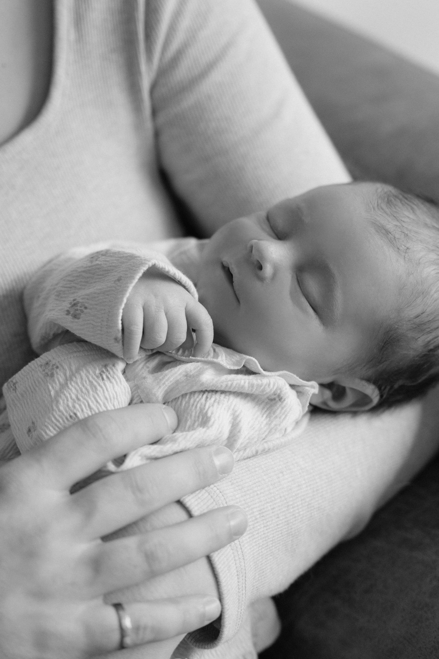 Close-up black and white photo of a peaceful sleeping newborn baby cradled in mothers arms.