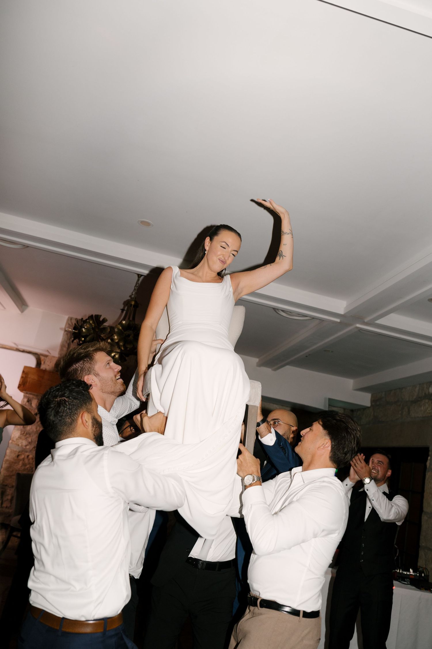 Bride in white dress lifted high by groomsmen during lively wedding reception celebration at Cambridge Mill.