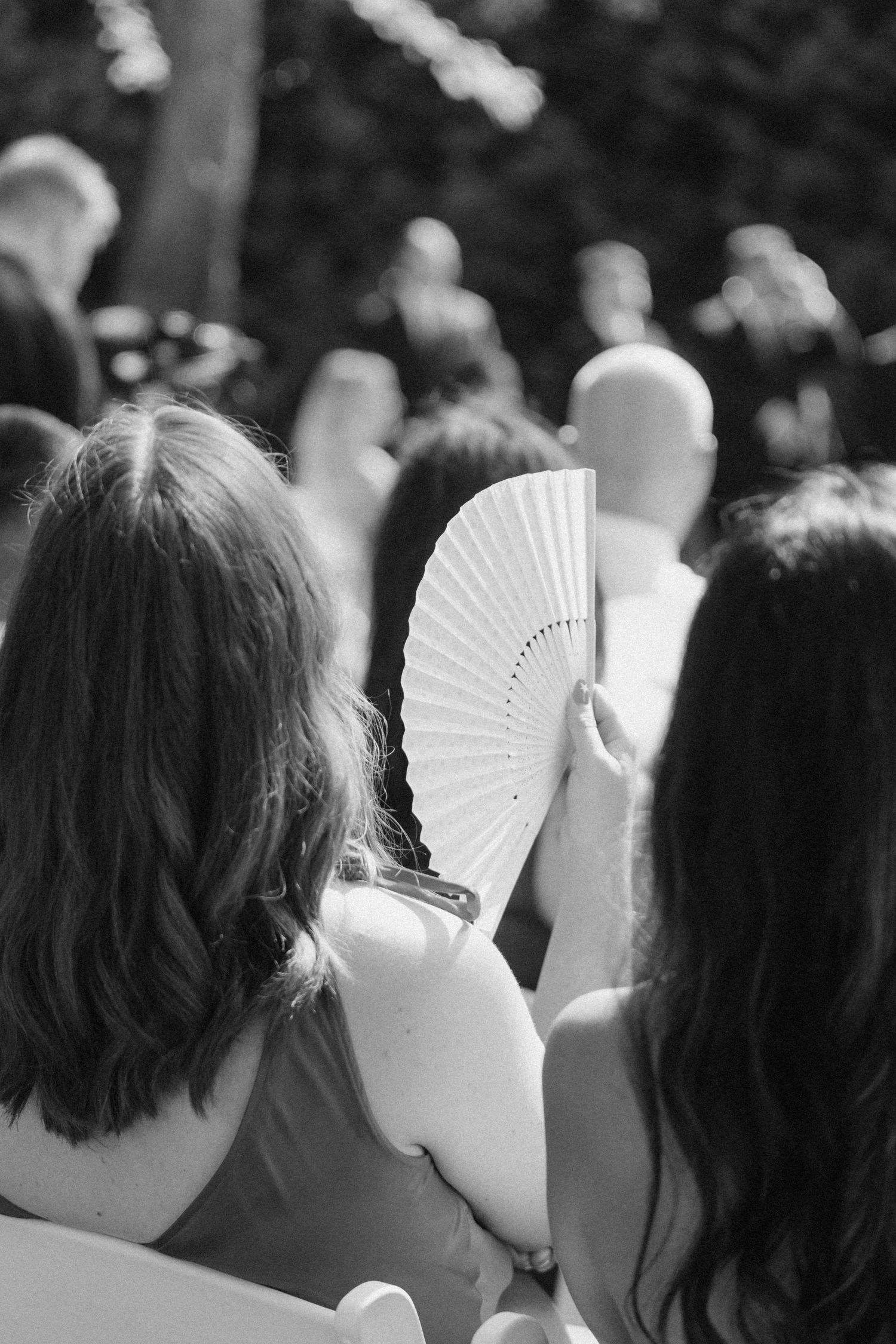 Black and white photo of wedding guests seated outside, woman holding decorative white hand fan.