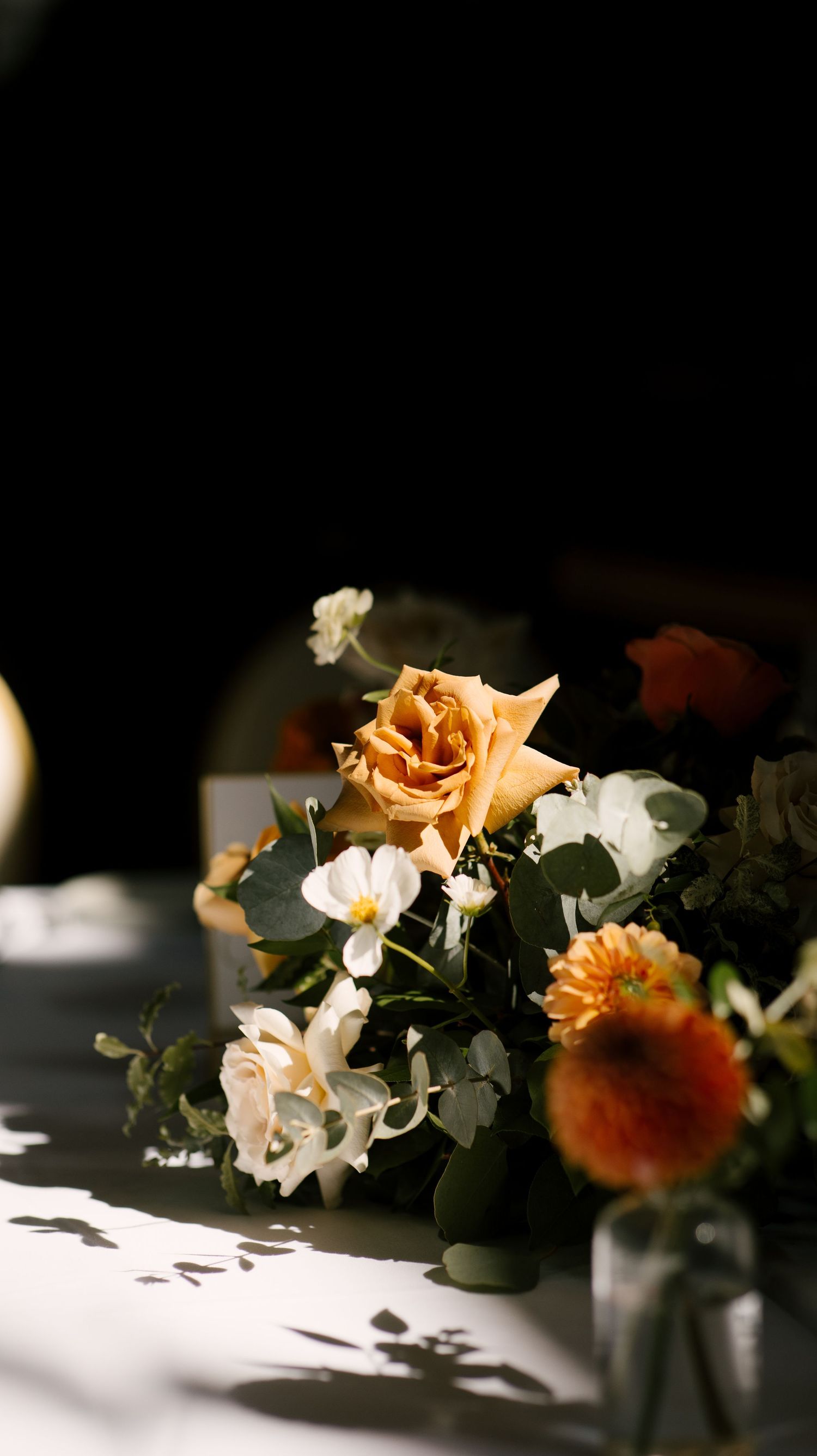 Elegant wedding floral arrangement featuring peach roses, white blooms, and greenery in dramatic moody lighting.