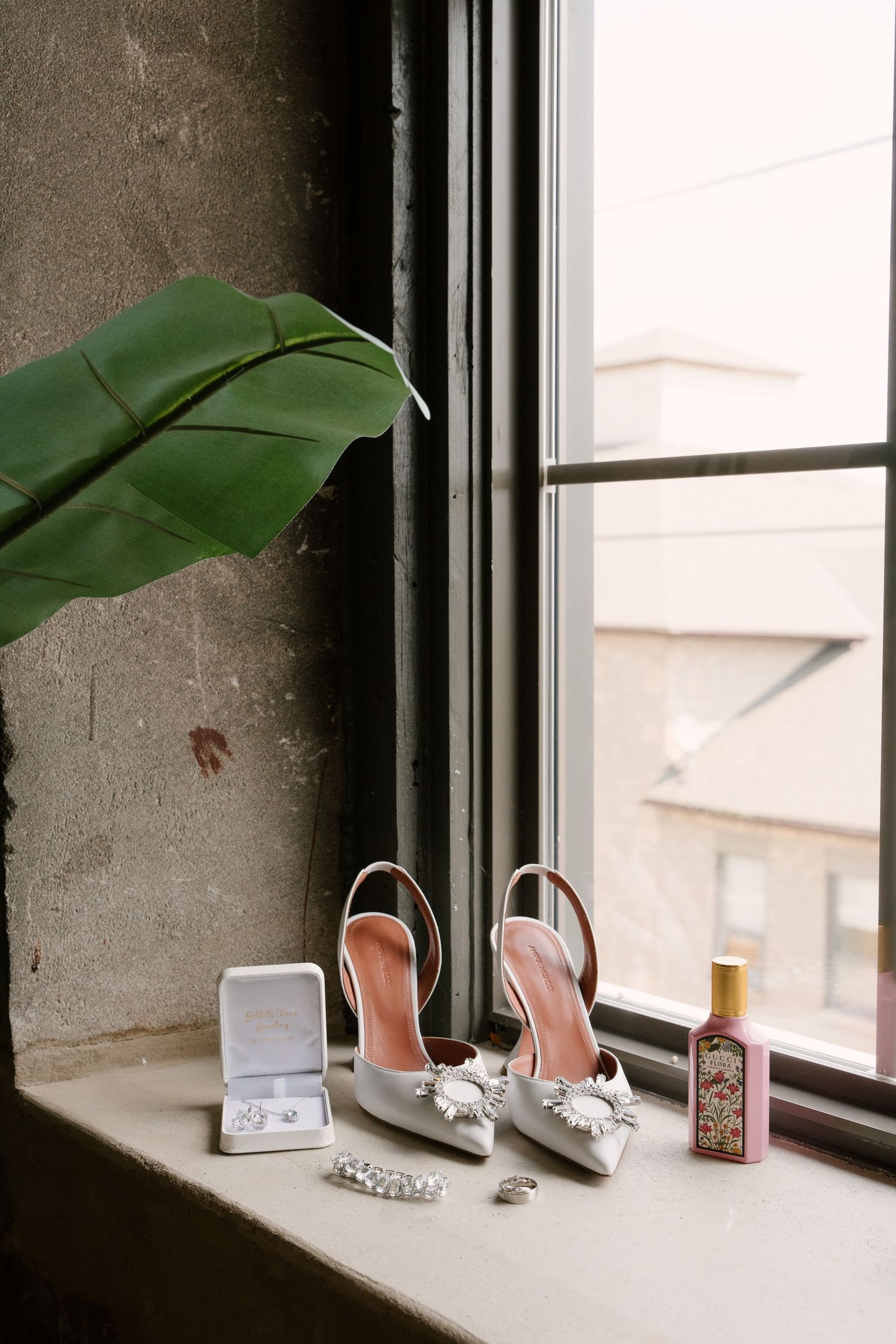 Bridal accessories arranged on window ledge including embellished heels, earrings, bracelet, ring and Gucci perfume.