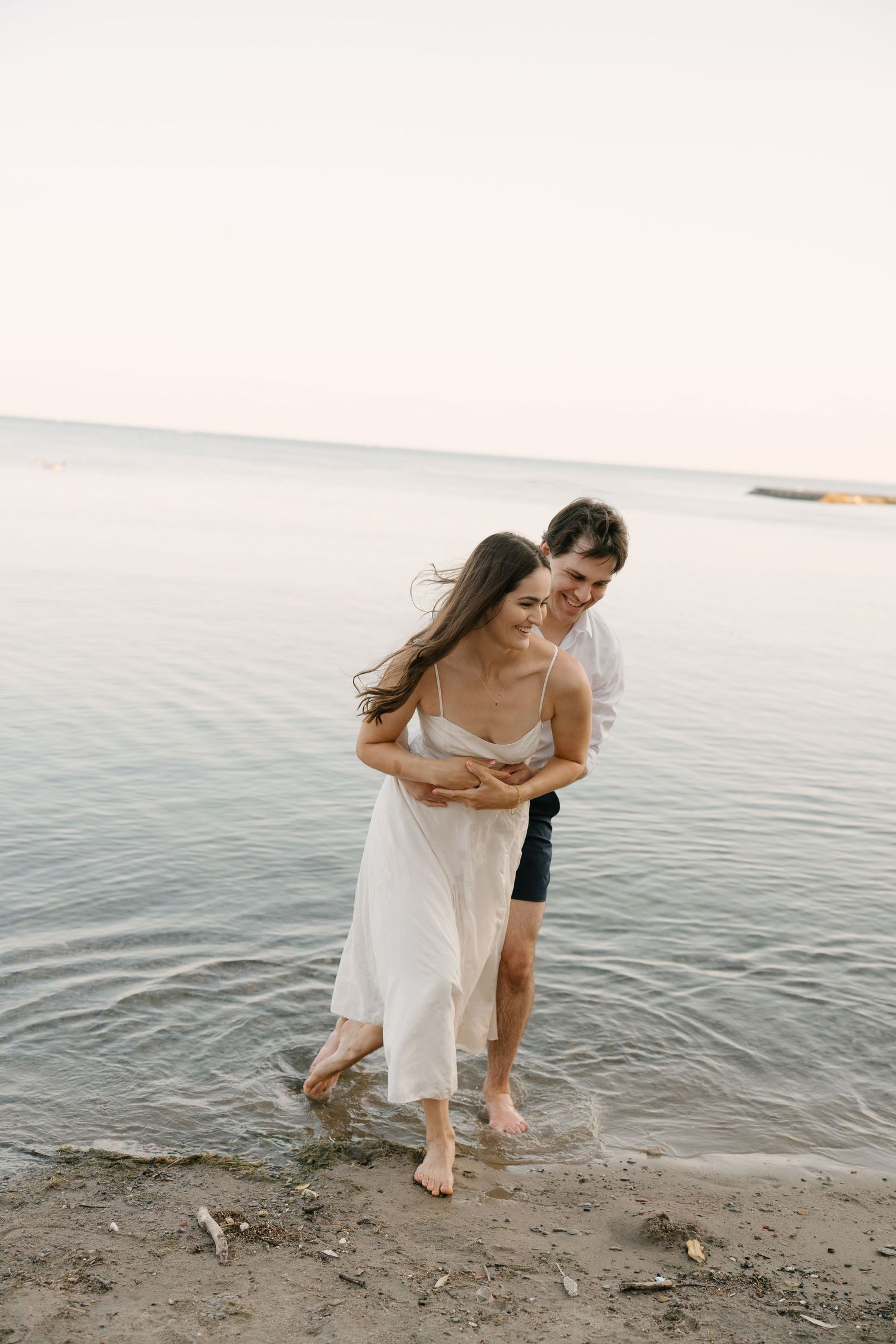 Couple embracing barefoot at the waters edge on a calm beach at dusk.