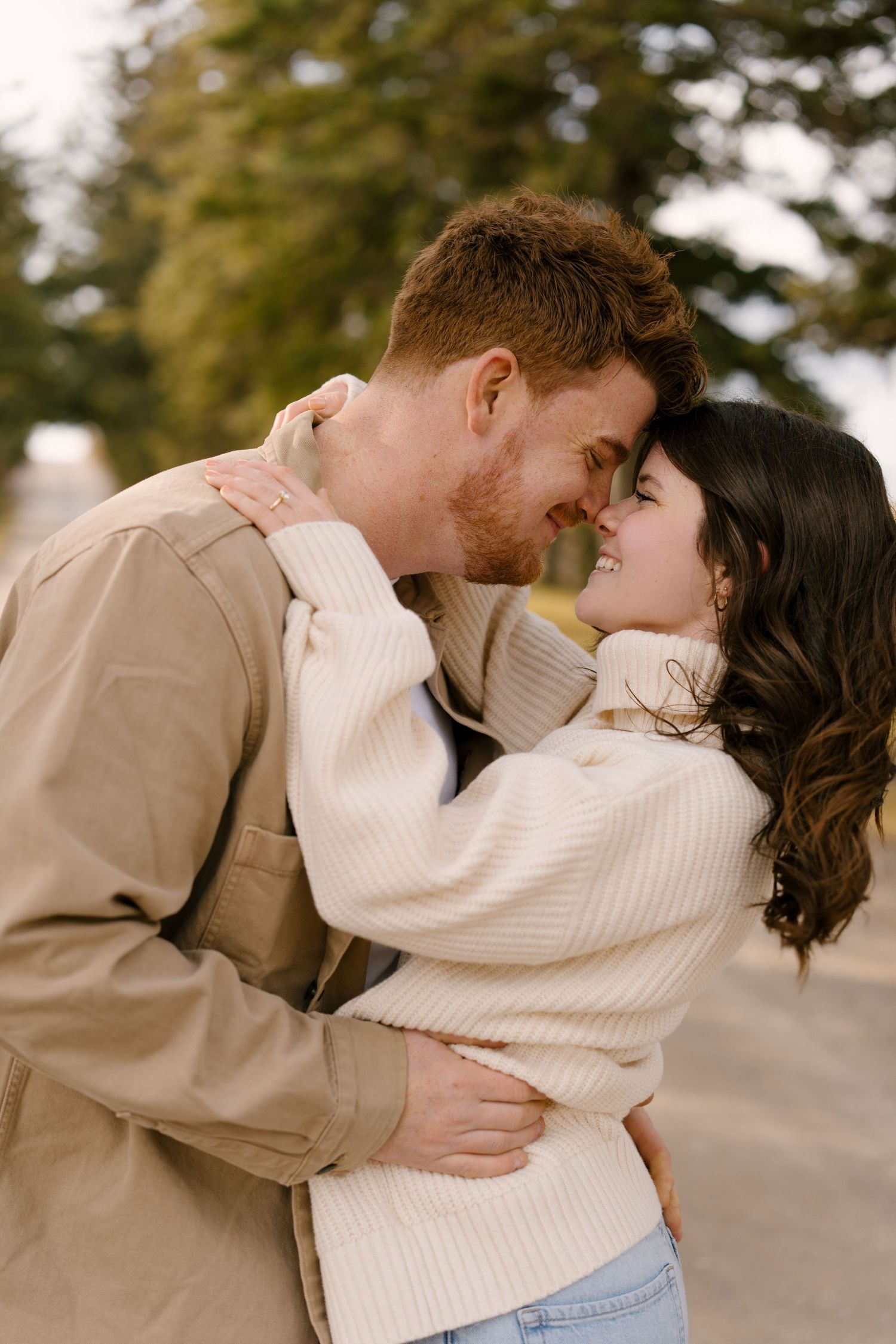Happy couple hugging closely on a scenic road, woman in white turtleneck wraps arms around mans neck.