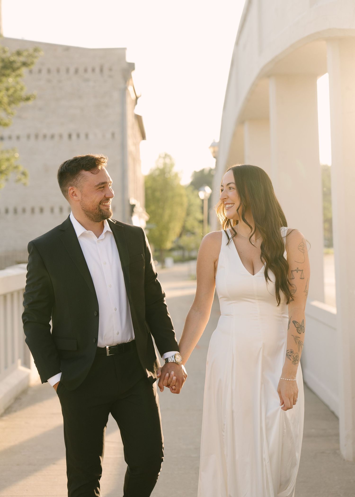 Couple holding hands and smiling at each other during golden hour engagement photos outdoors.