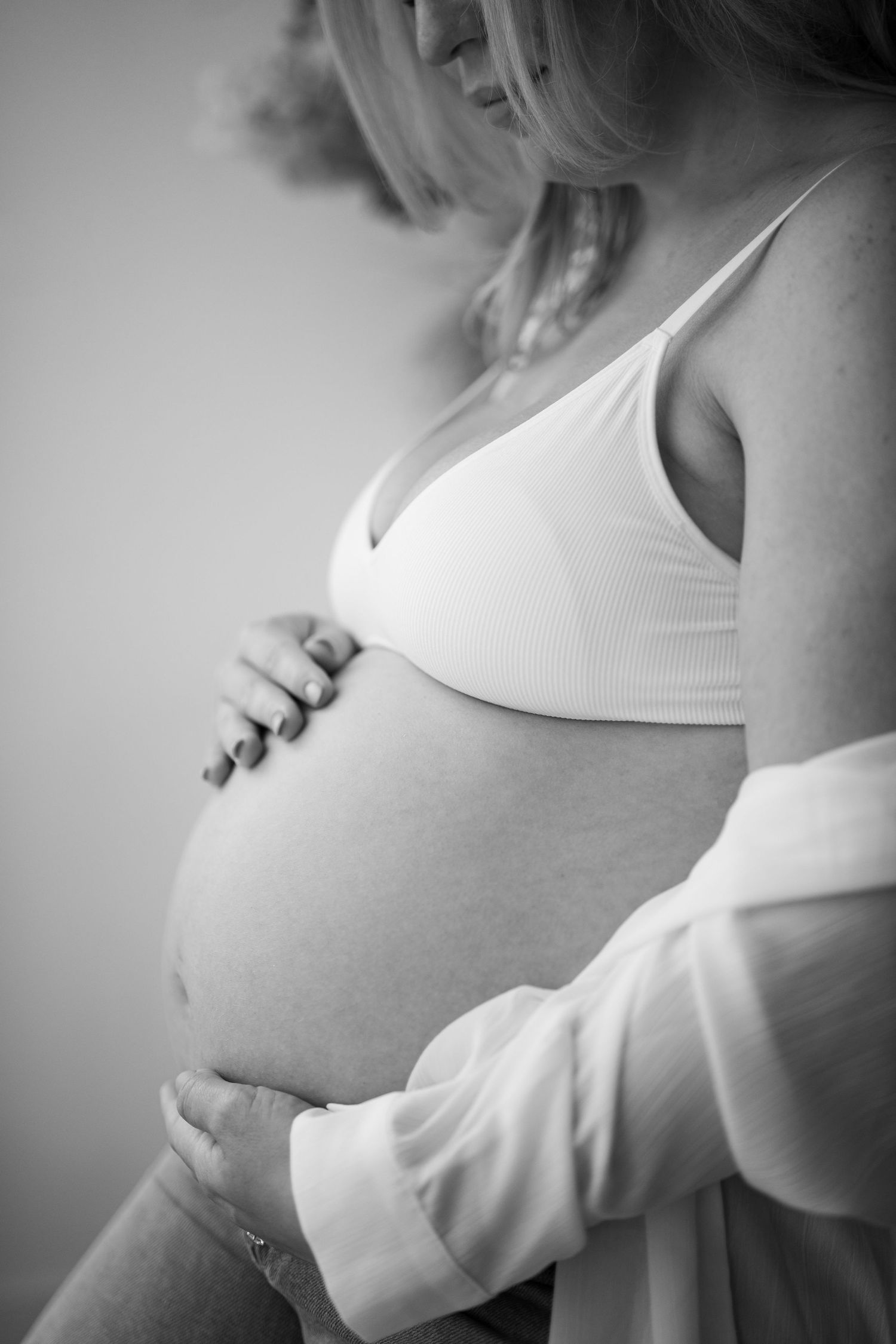 Black and white photo of a pregnant woman cradling her bare baby bump with both hands.
