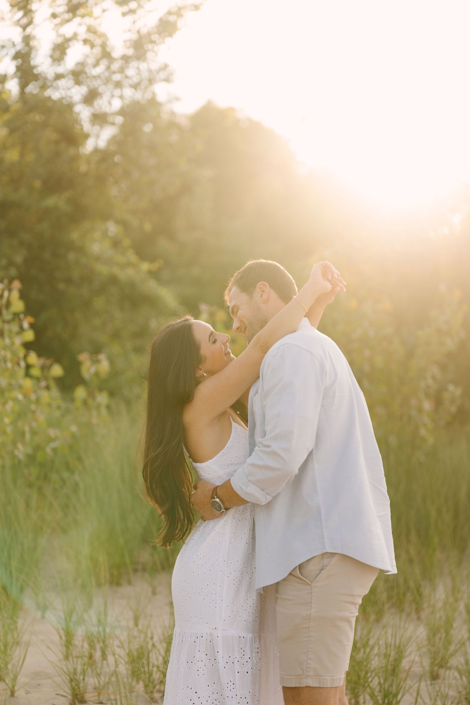 Couple embracing romantically in warm golden sunlight surrounded by lush green foliage.
