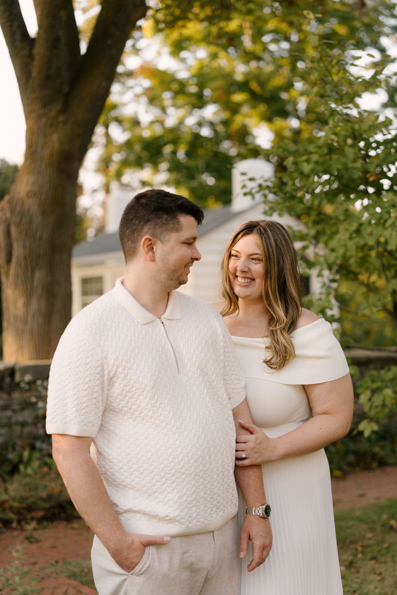 Smiling couple in coordinating white outfits standing together in a golden-hour garden setting.