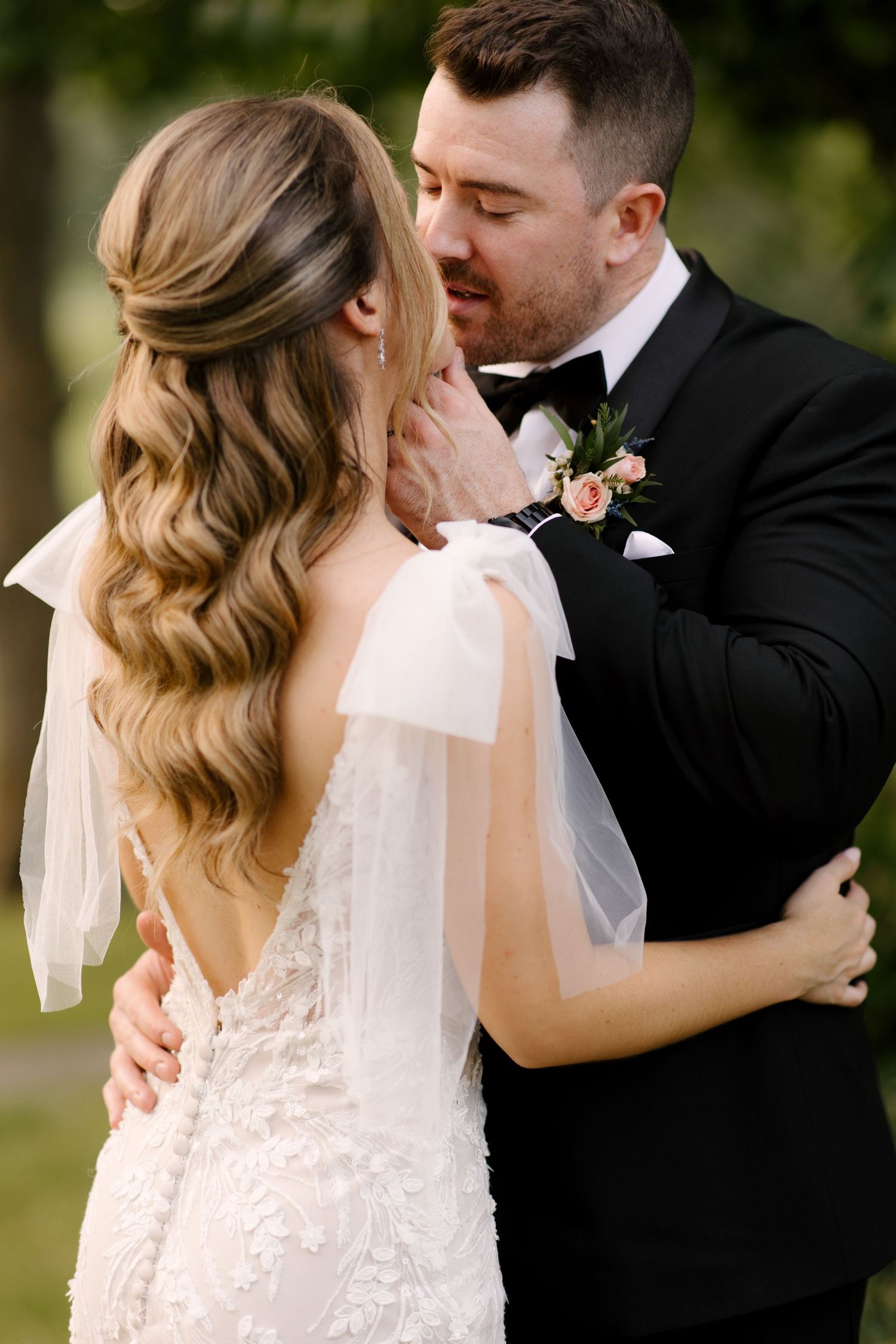 Bride and groom sharing a romantic moment, she in lace gown with veil, he in black tuxedo with floral boutonniere.
