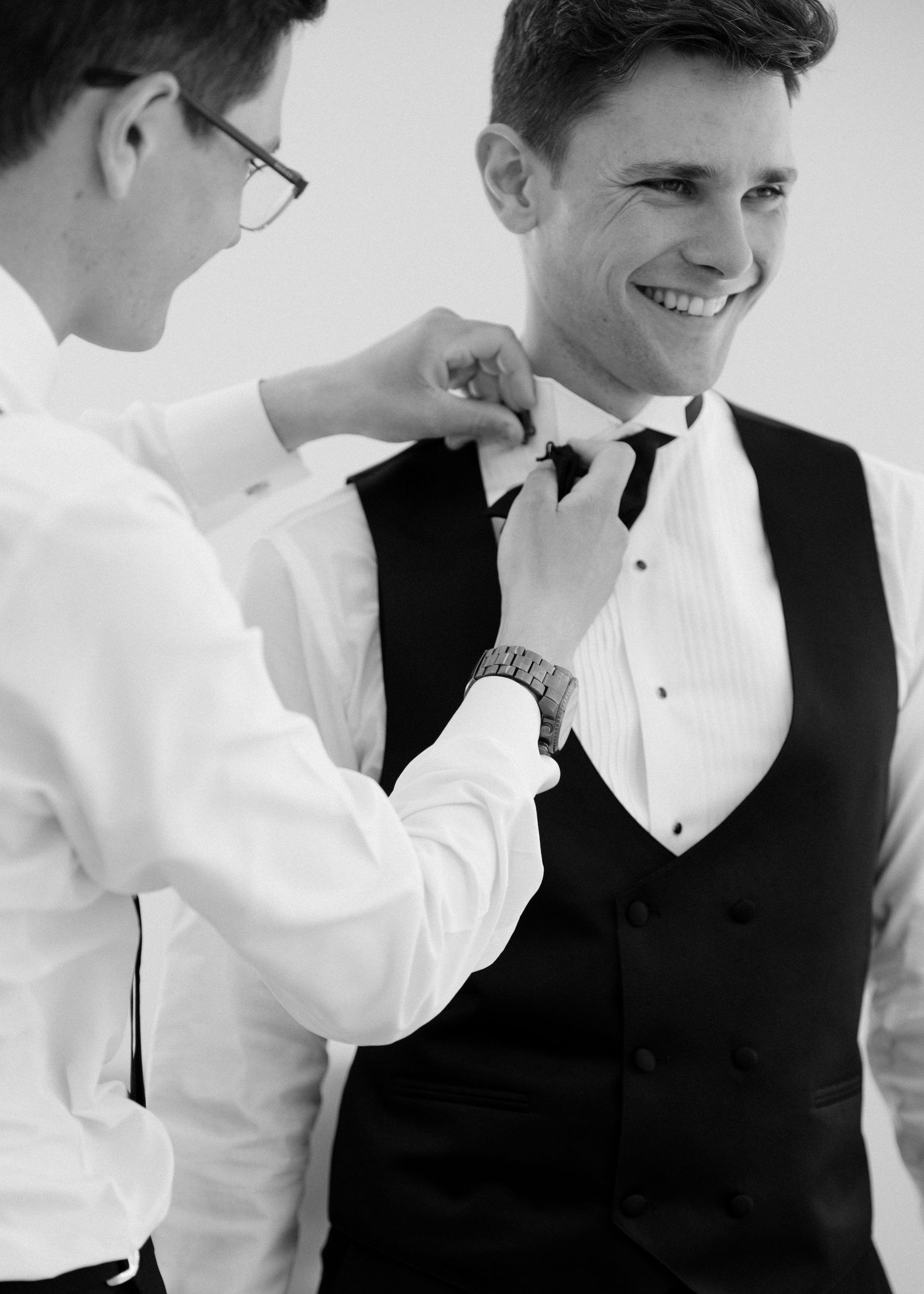 Black and white photo of groomsman adjusting the grooms bow tie before the wedding at Roseville Estates wedding venue.