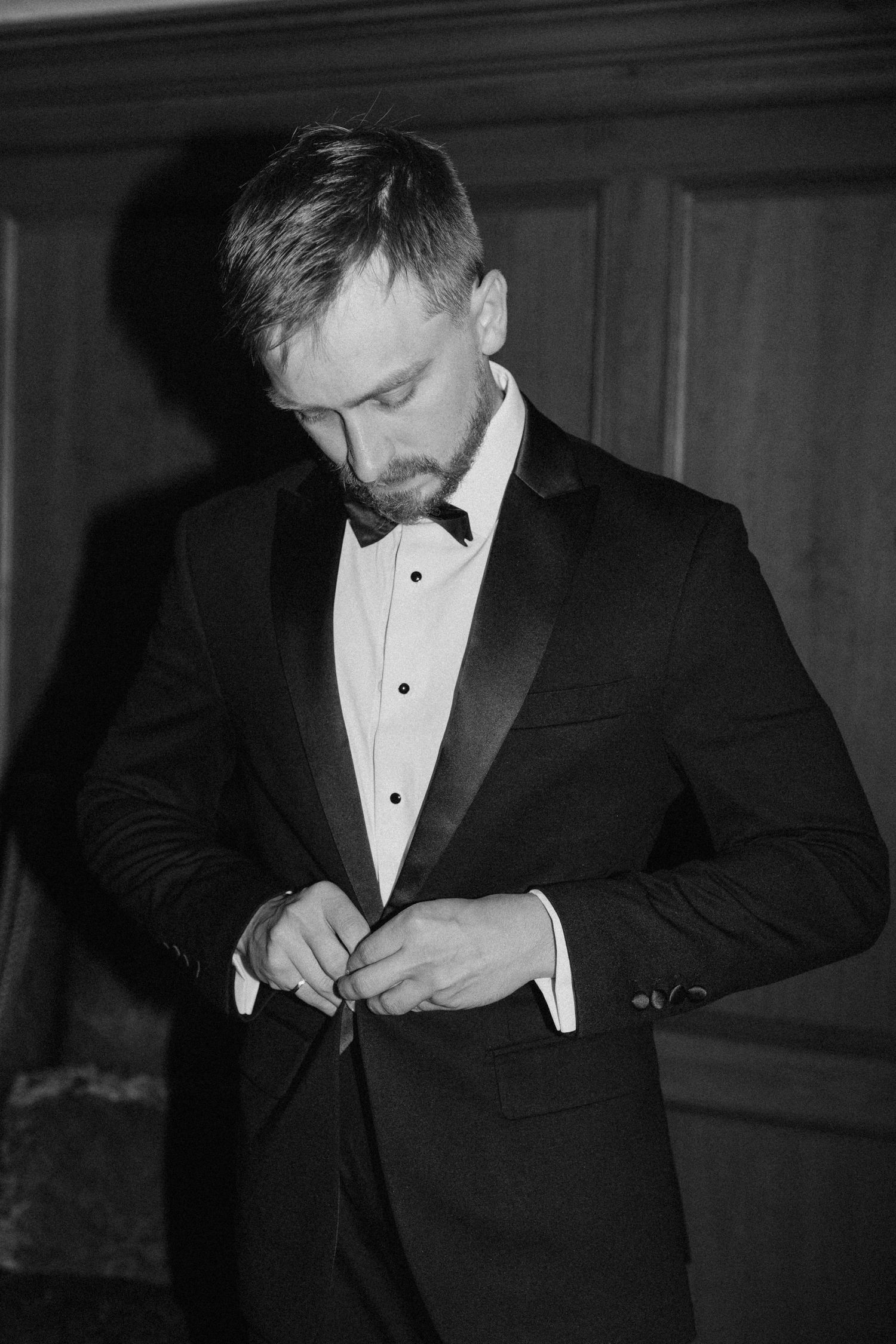 Dapper groom buttoning his black tuxedo jacket in a classic black and white portrait  at Pillar and Post.