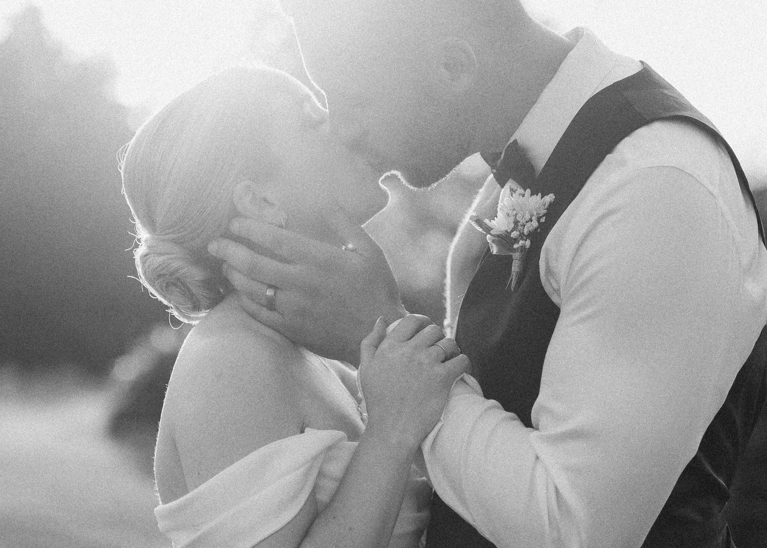 Black and white romantic close-up of bride and groom sharing a kiss in soft backlit sunlight.