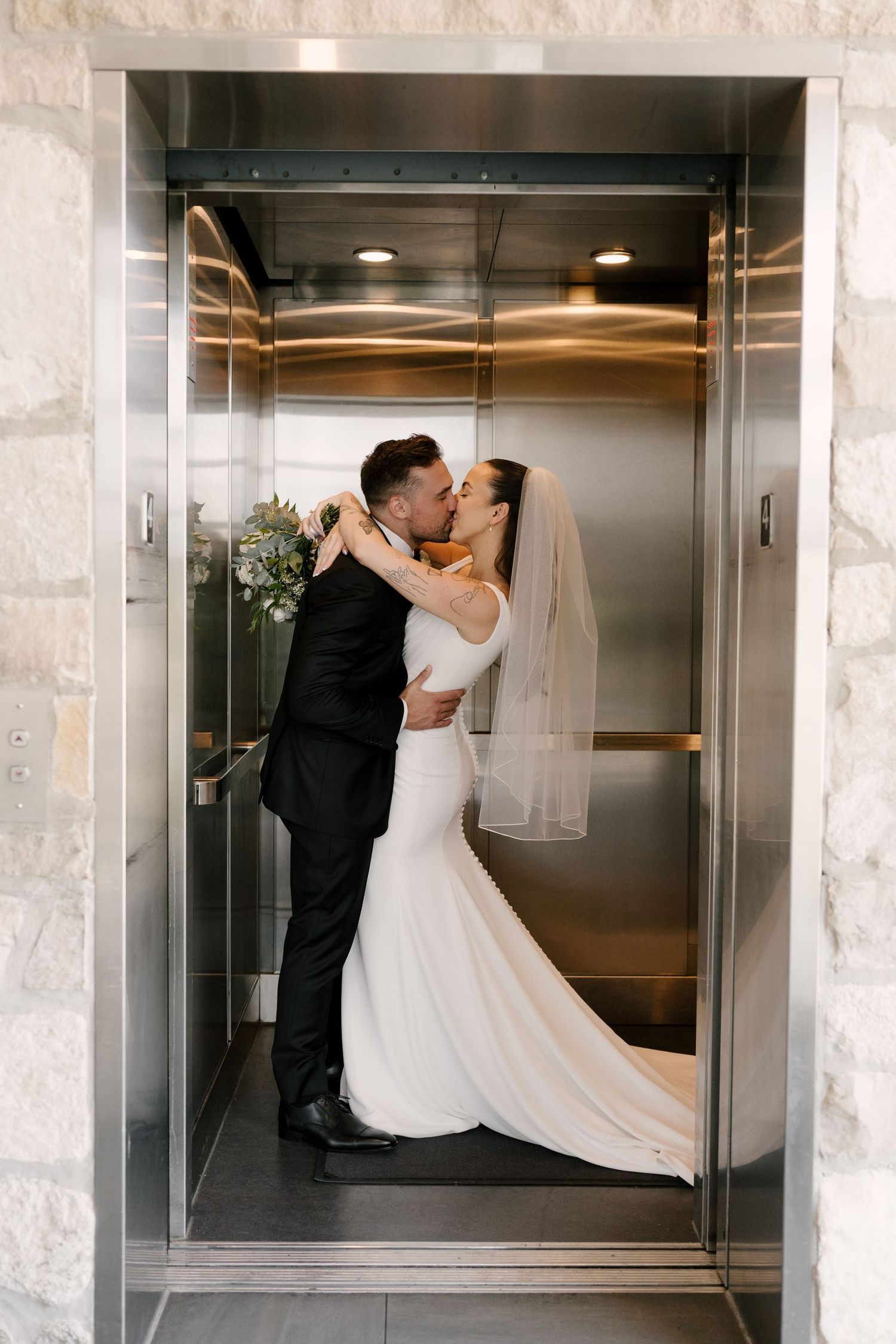 Bride and groom share a passionate kiss inside a gold elevator on their wedding day.
