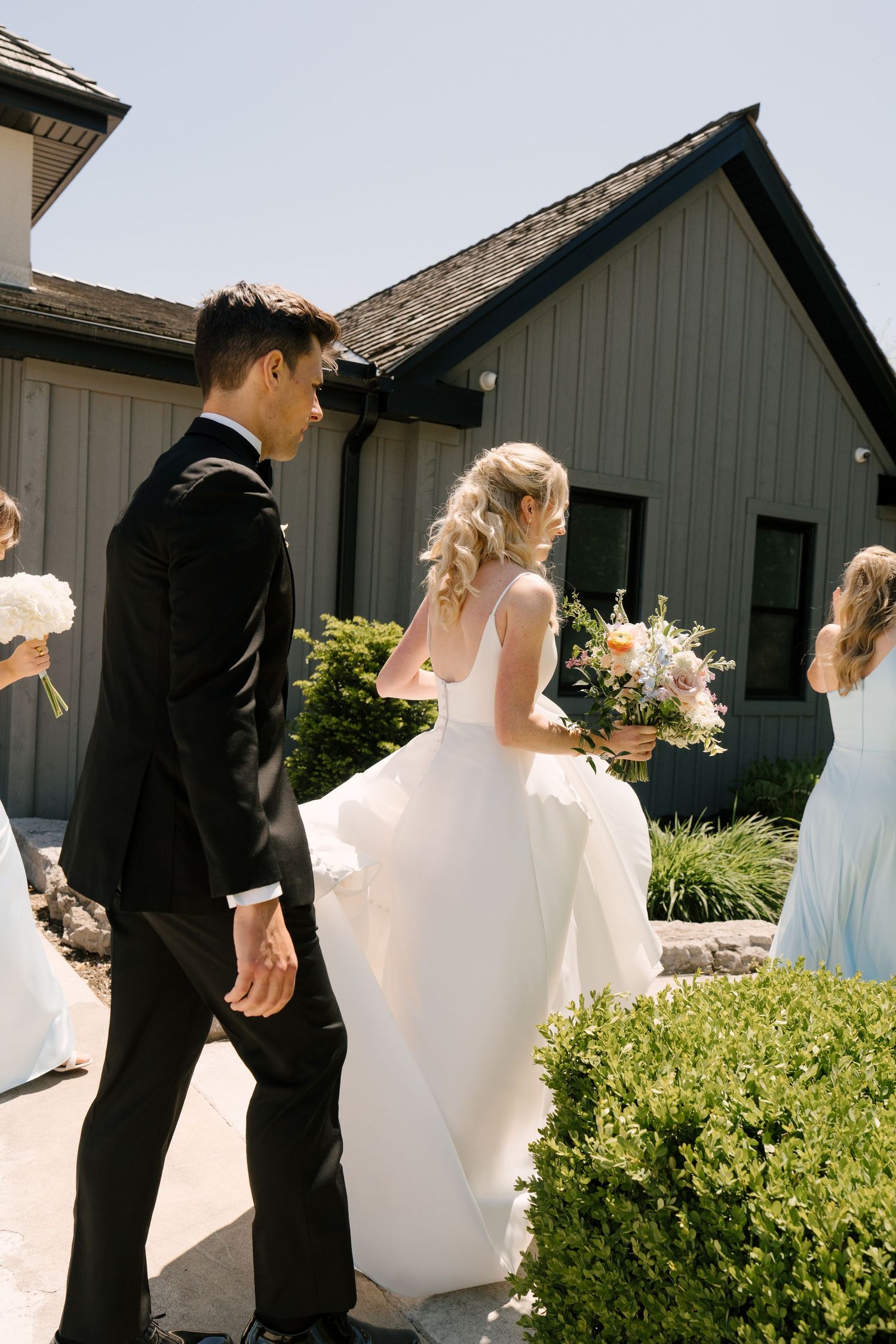 Groom in black suit walks beside bride in white gown carrying colourful bouquet near Roseville Estates wedding venue.