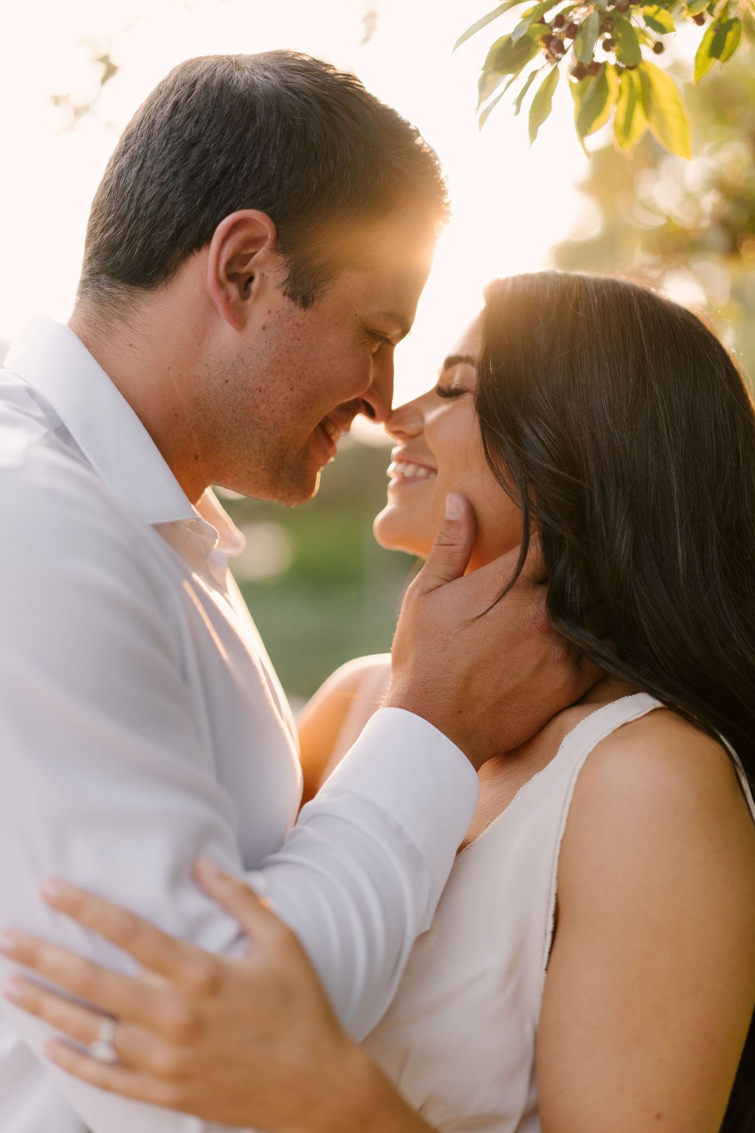 Romantic couple nearly kissing in golden sunset light, man tenderly holding woman's face outdoors.