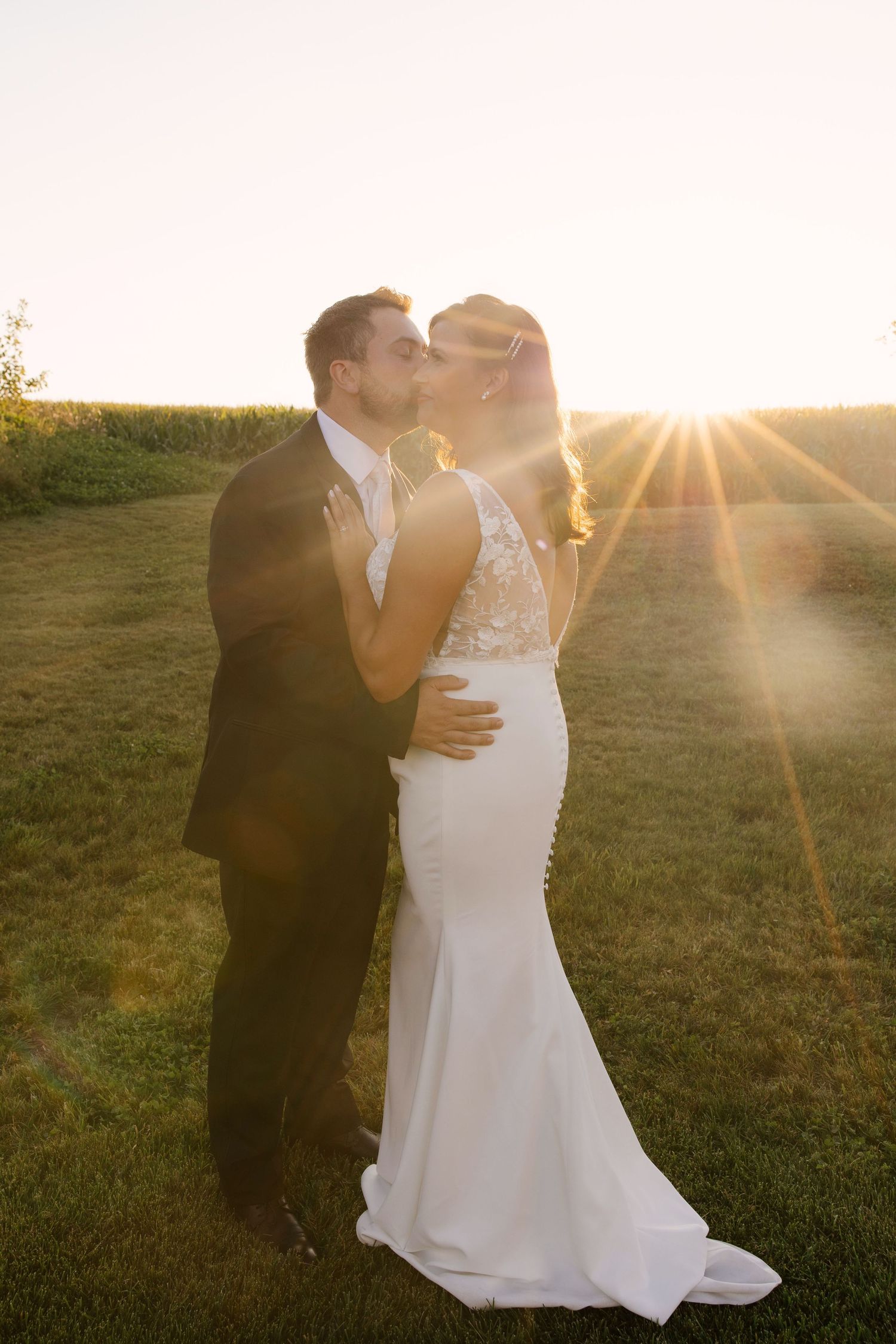 Bride and groom embracing in a passionate kiss with beautiful sun flare at golden hour.