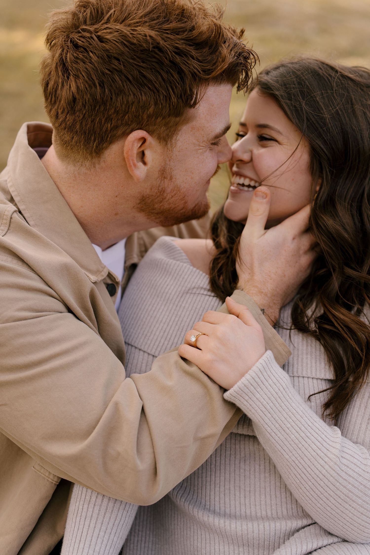 Couple sharing an intimate moment, smiling close together outdoors, woman wearing engagement ring.