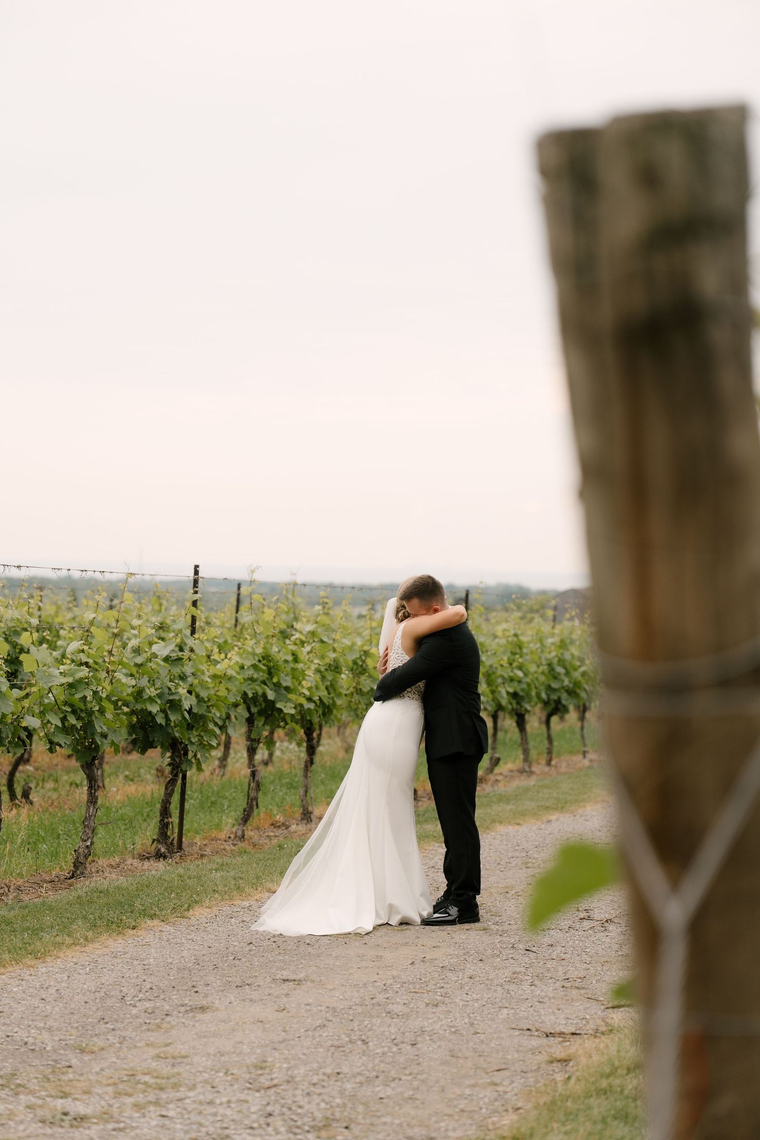 Bride and groom embrace in a scenic vineyard pathway on their wedding day at Niagara on the lake.