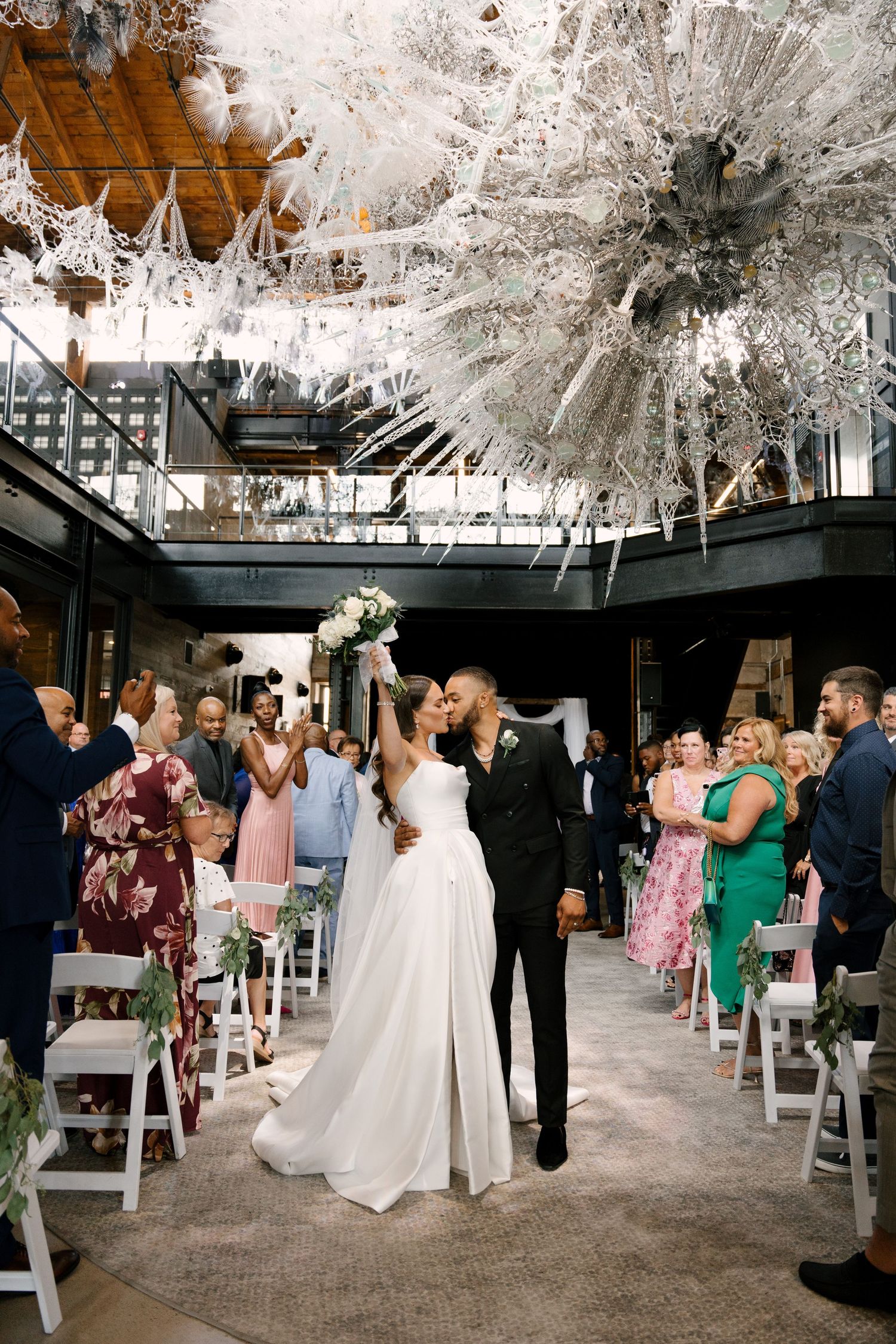 Bride and groom share a kiss while walking down the aisle at an elegant indoor Tapestry Hall wedding ceremony.