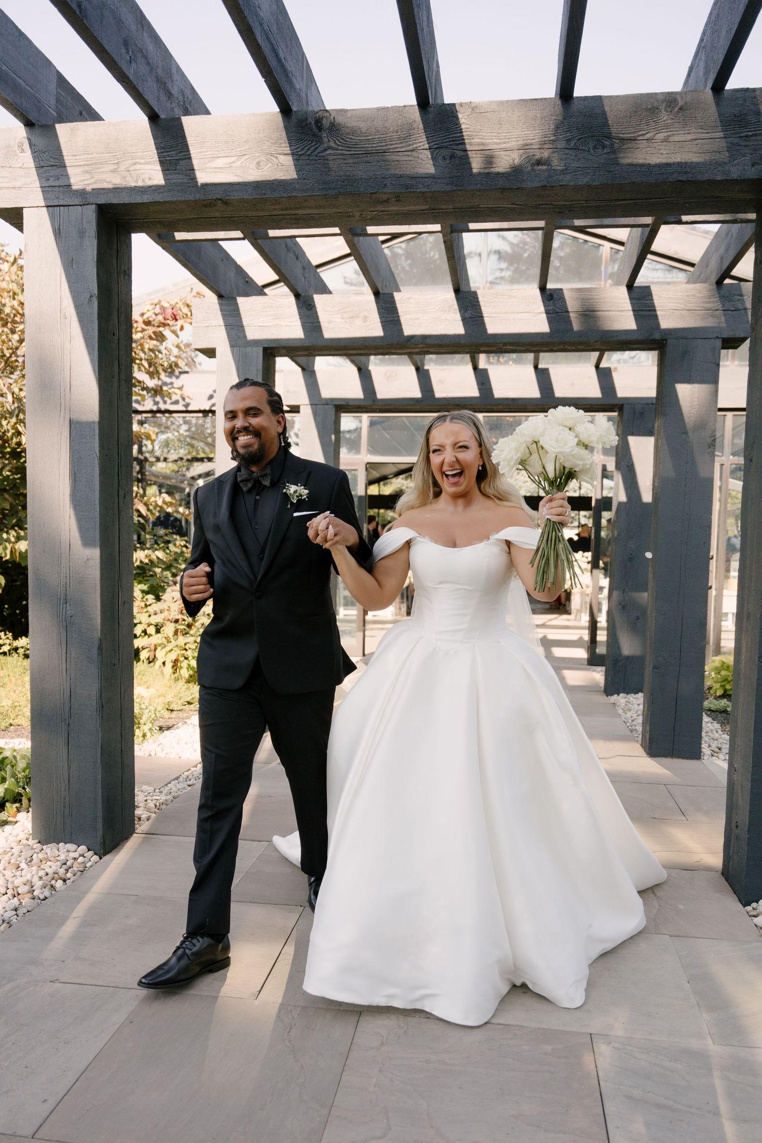 Joyful bride and groom celebrate under wooden pergola after wedding ceremony at Whistle Bear venue.