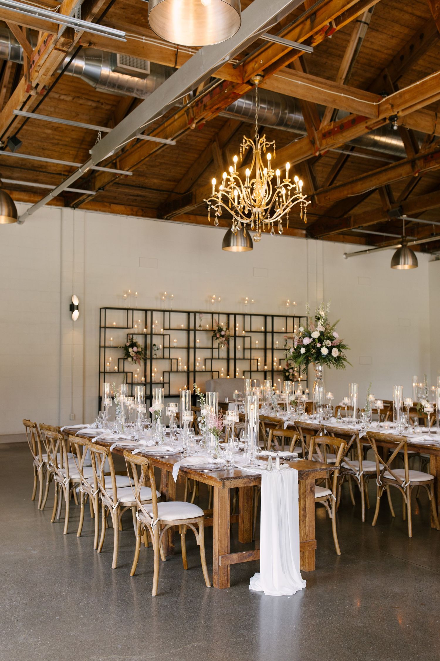 Elegant wedding reception with long wooden tables, cross-back chairs, chandelier, candles, and floral centerpieces in St Marys Venue.